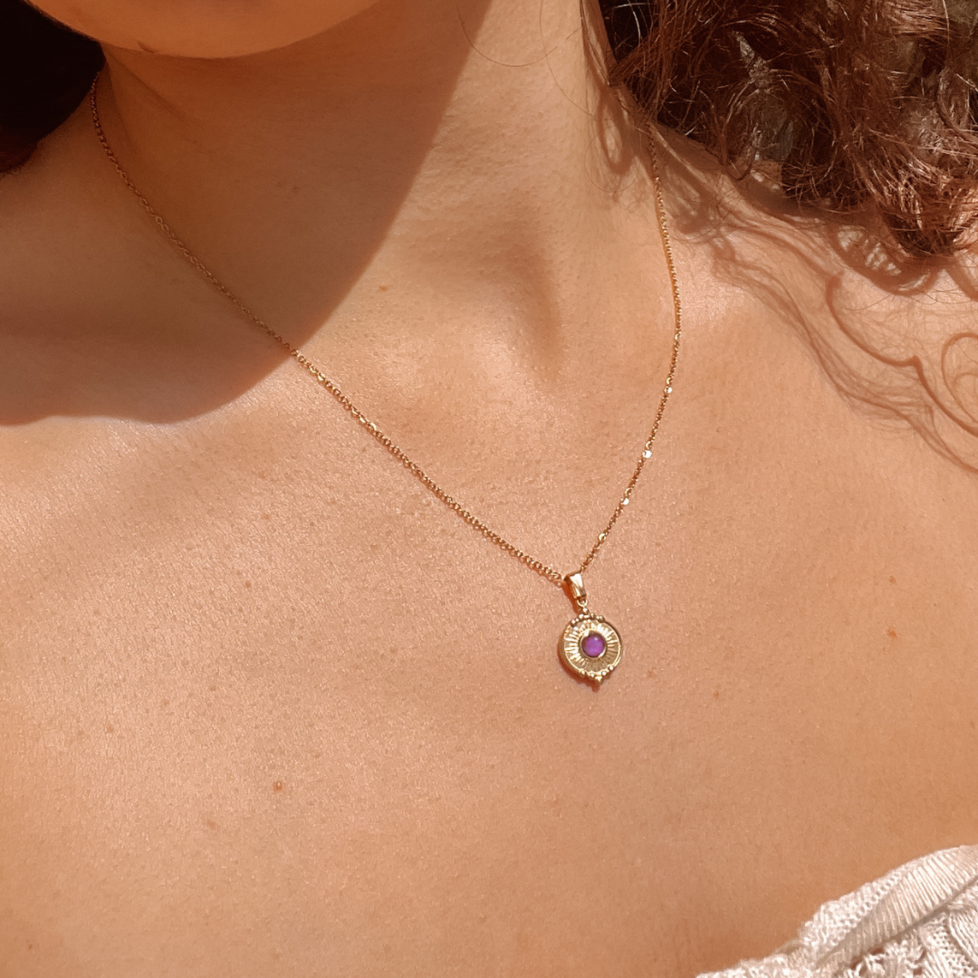 Winziger runder lila Amethyst-Anhänger an feiner Goldkette, am Hals eines Modells gezeigt.