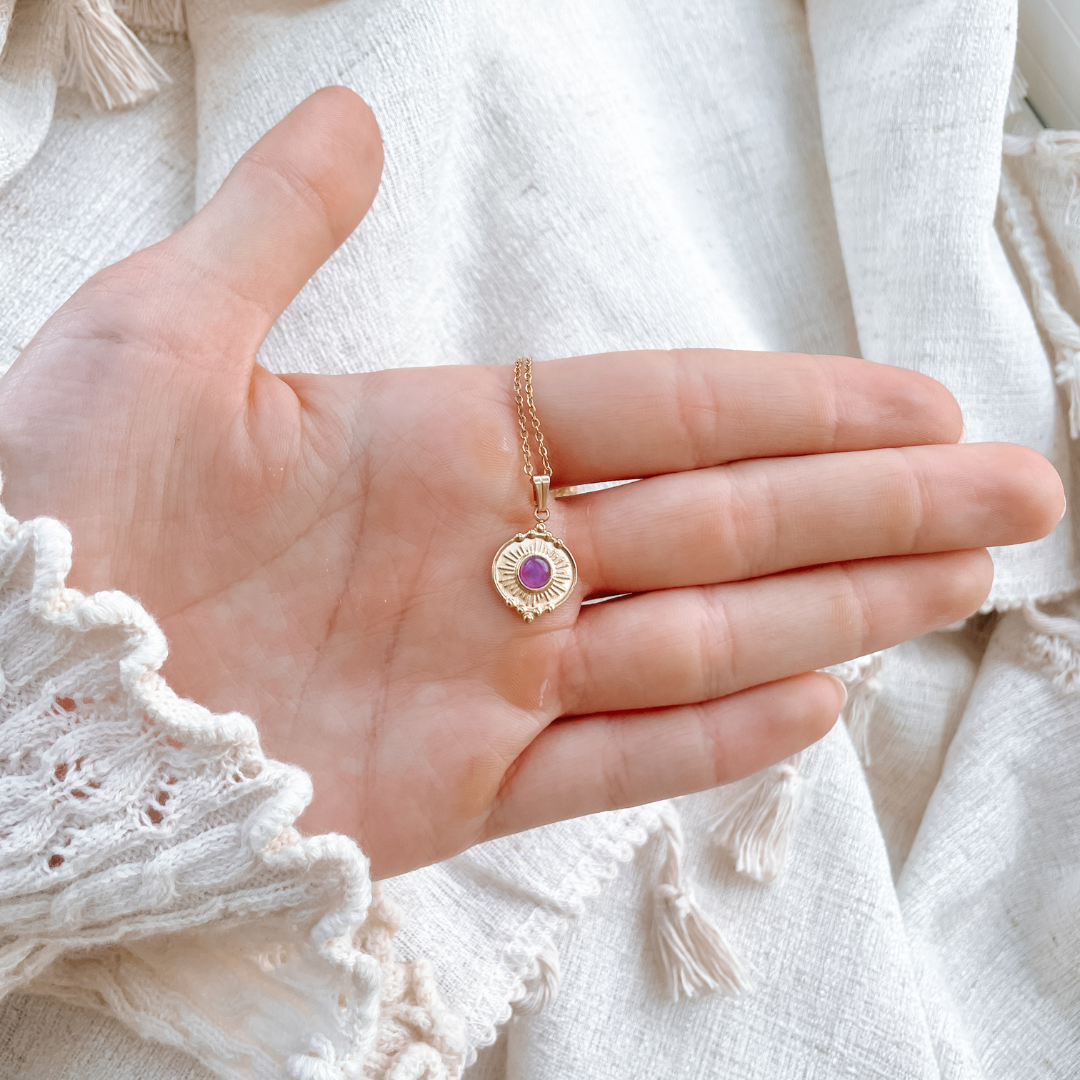 Handgemachte lila Amethyst-Kette mit rundem Münze Anhänger in Gold, liegend auf Hand