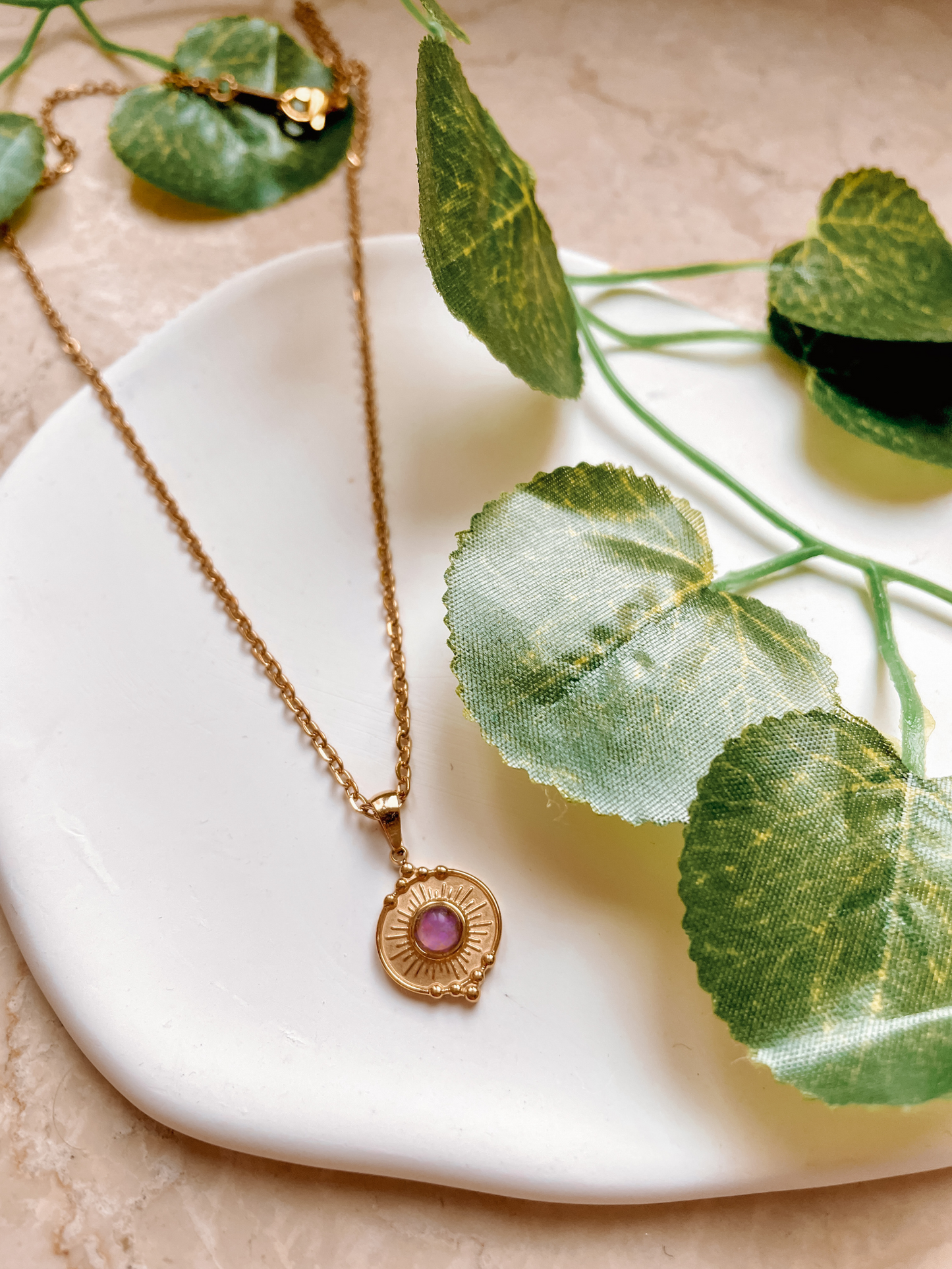Handgemachte lila Amethyst-Kette mit rundem filigranen Anhänger in Gold, liegend auf Tablett