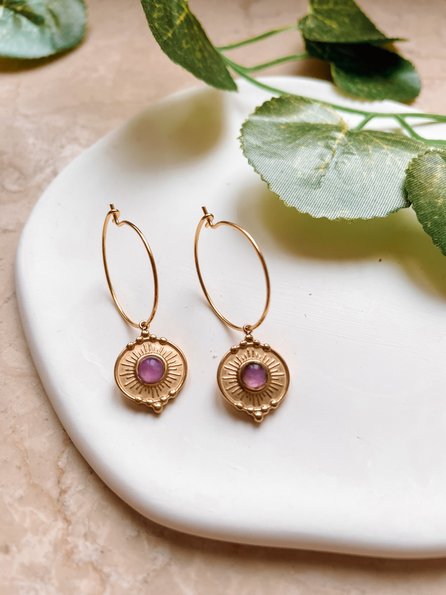 Goldene Creolen-Ohrringe mit filigranen Fassungen und runden, lila Amethyst-Steinen auf Tablett