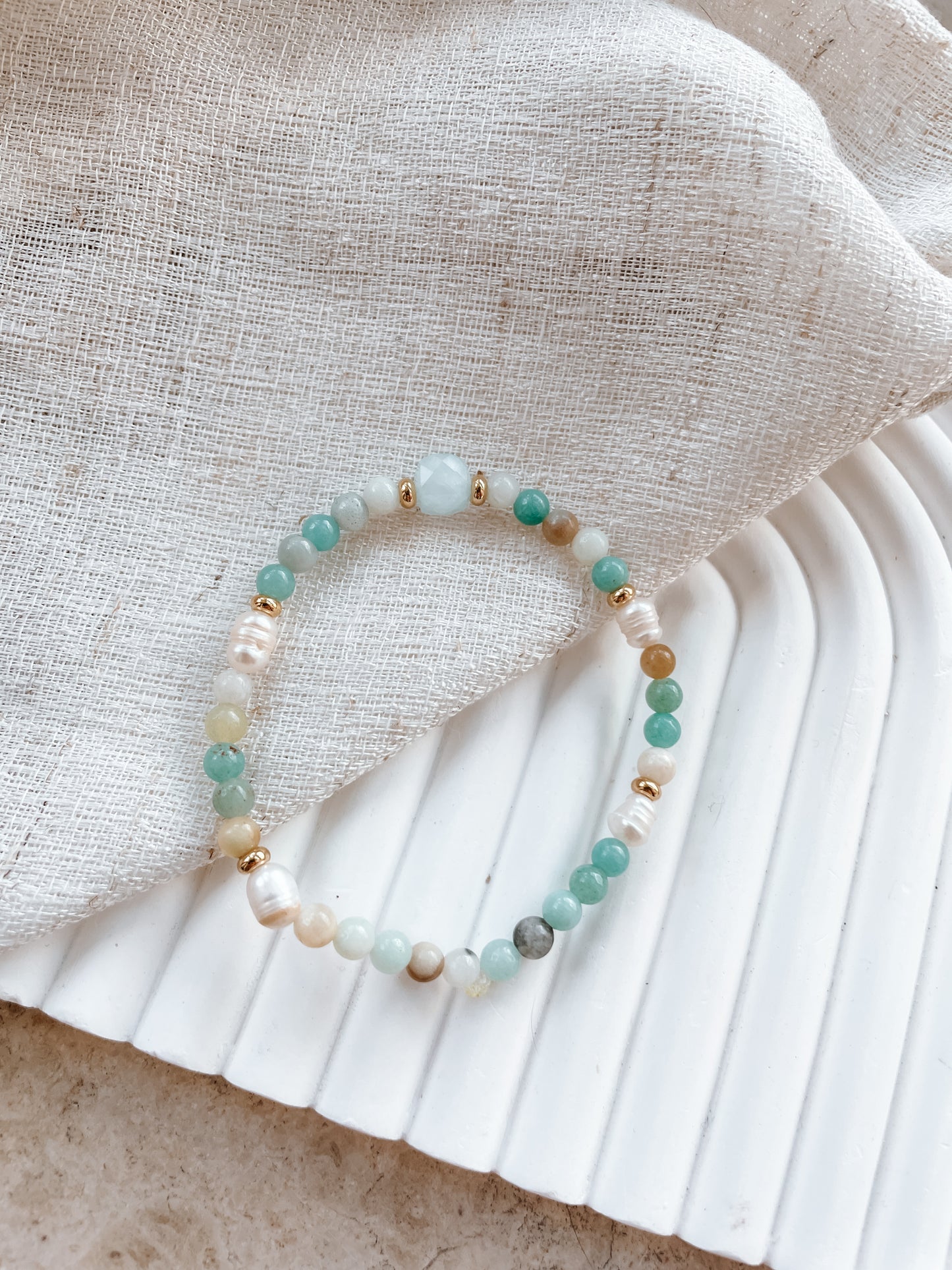 Blaues Amazonit-Perlenarmband in Gold mit Aquamarin Stein liegend auf Tuch
