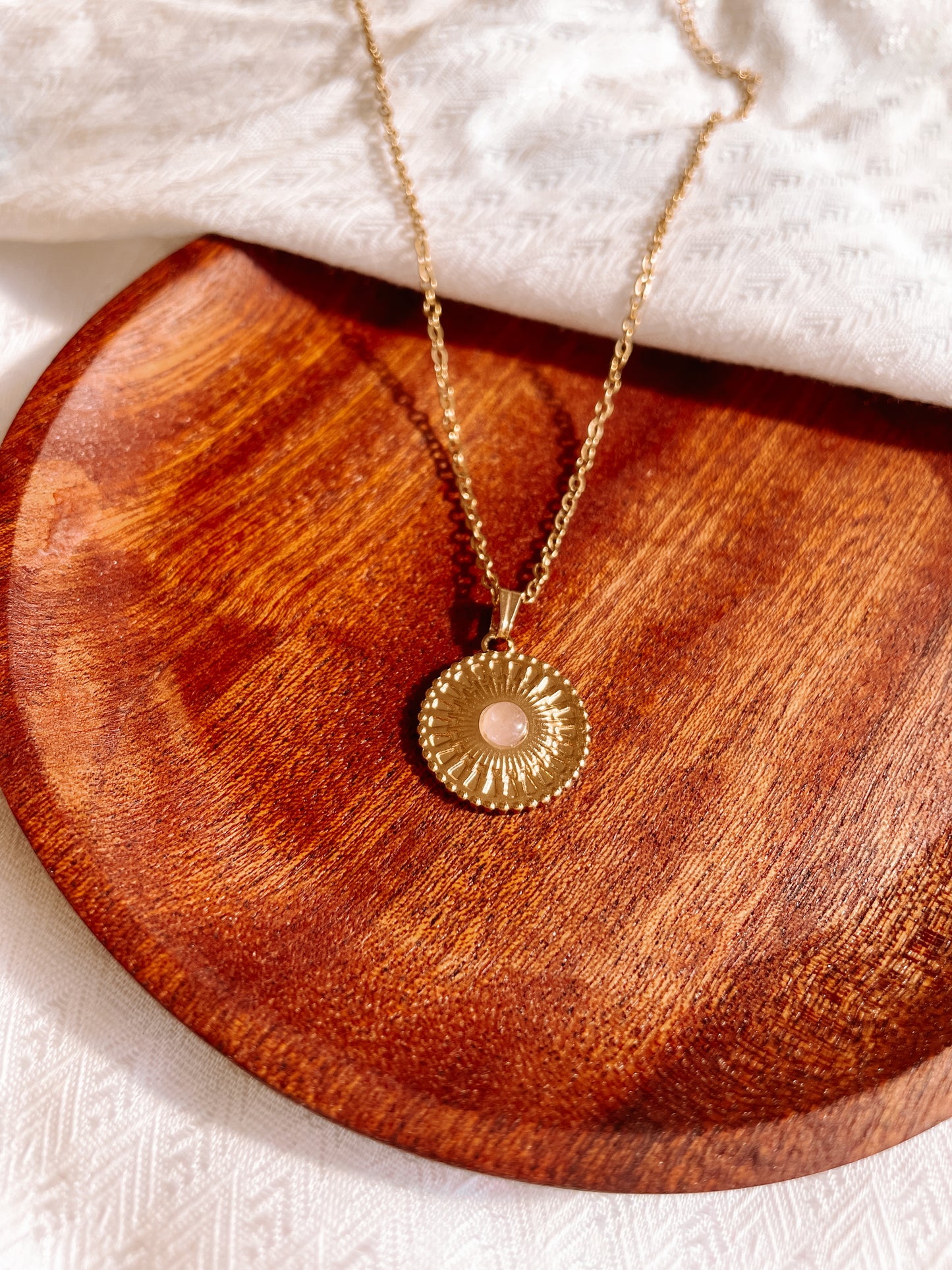 Handgemachte rosa Rosenquarz-Kette mit rundem Medaillon Anhänger in Gold, liegend auf Tablett