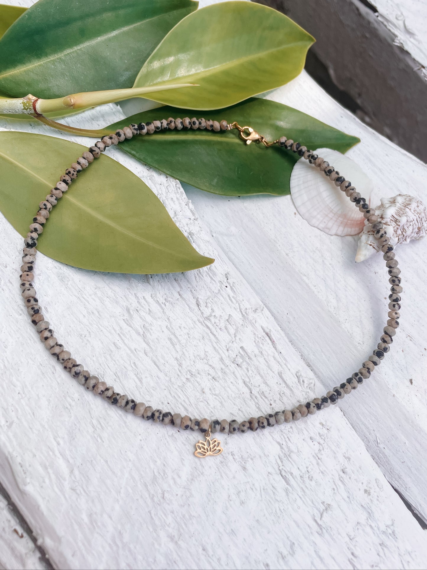 gepunktete Dalmatiner Jaspis-Perlenarmkette in Gold mit Lotusblume Anhänger liegend auf weißem Holz