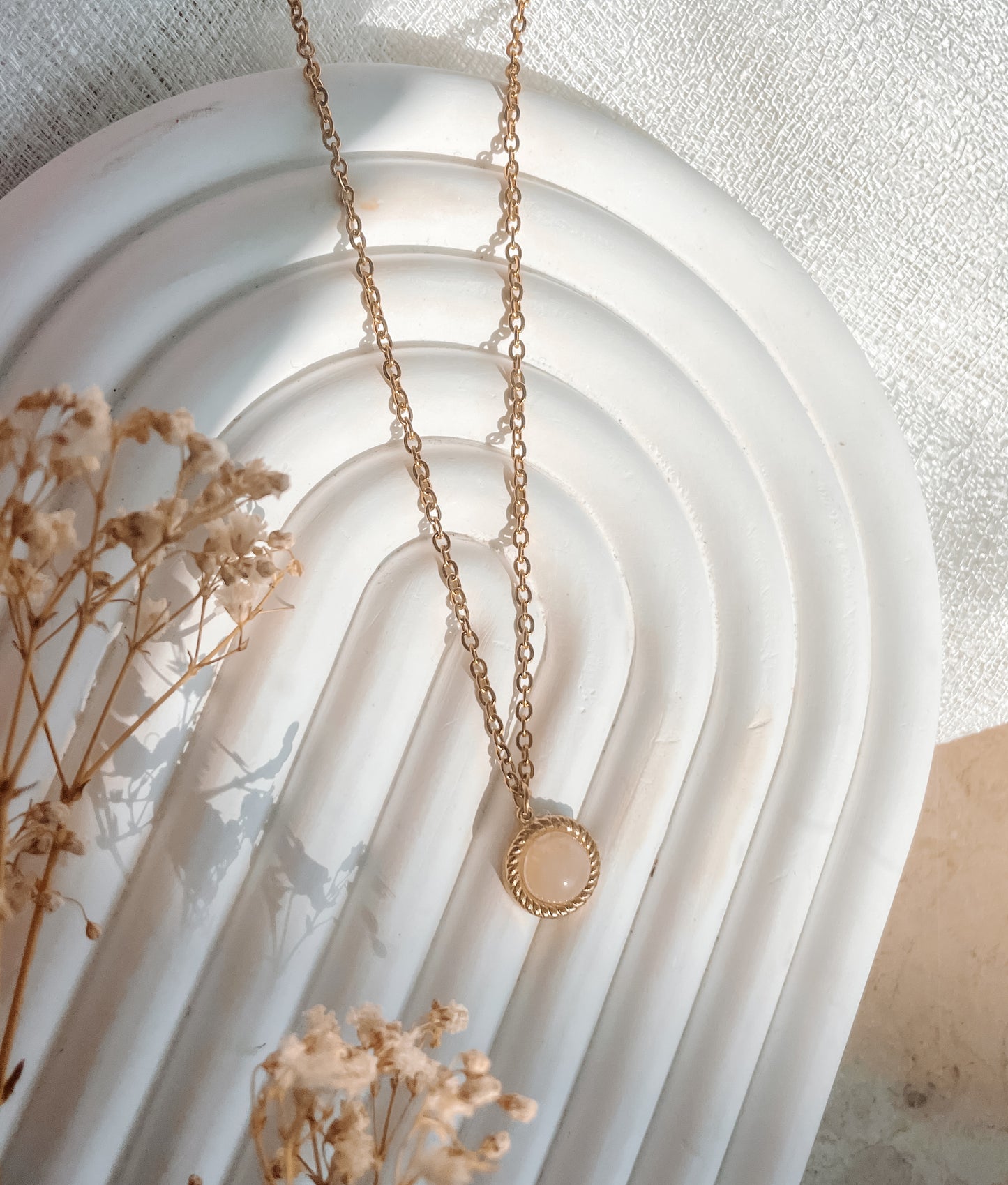 Handgemachte rosa Rosenquarz-Kette mit rundem Anhänger in Gold, liegend auf Tablett