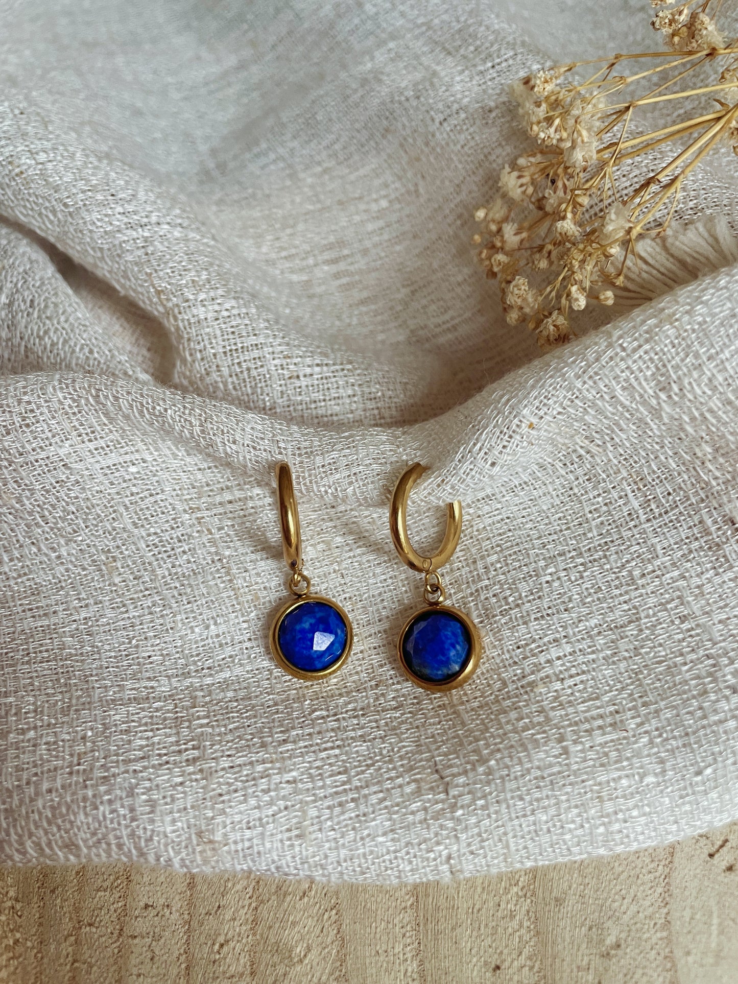 Goldene Creolen-Ohrringe mit runden, facettierten Lapis-Lazuli-Steinen auf weißem Tuch
