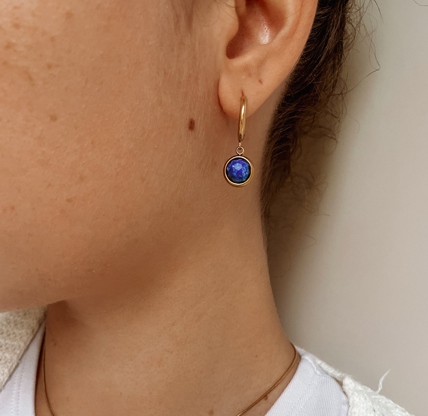 Goldene Creolen-Ohrringe mit runden, facettierten Lapis-Lazuli-Steinen an Ohr eines Modells, Detailaufnahme