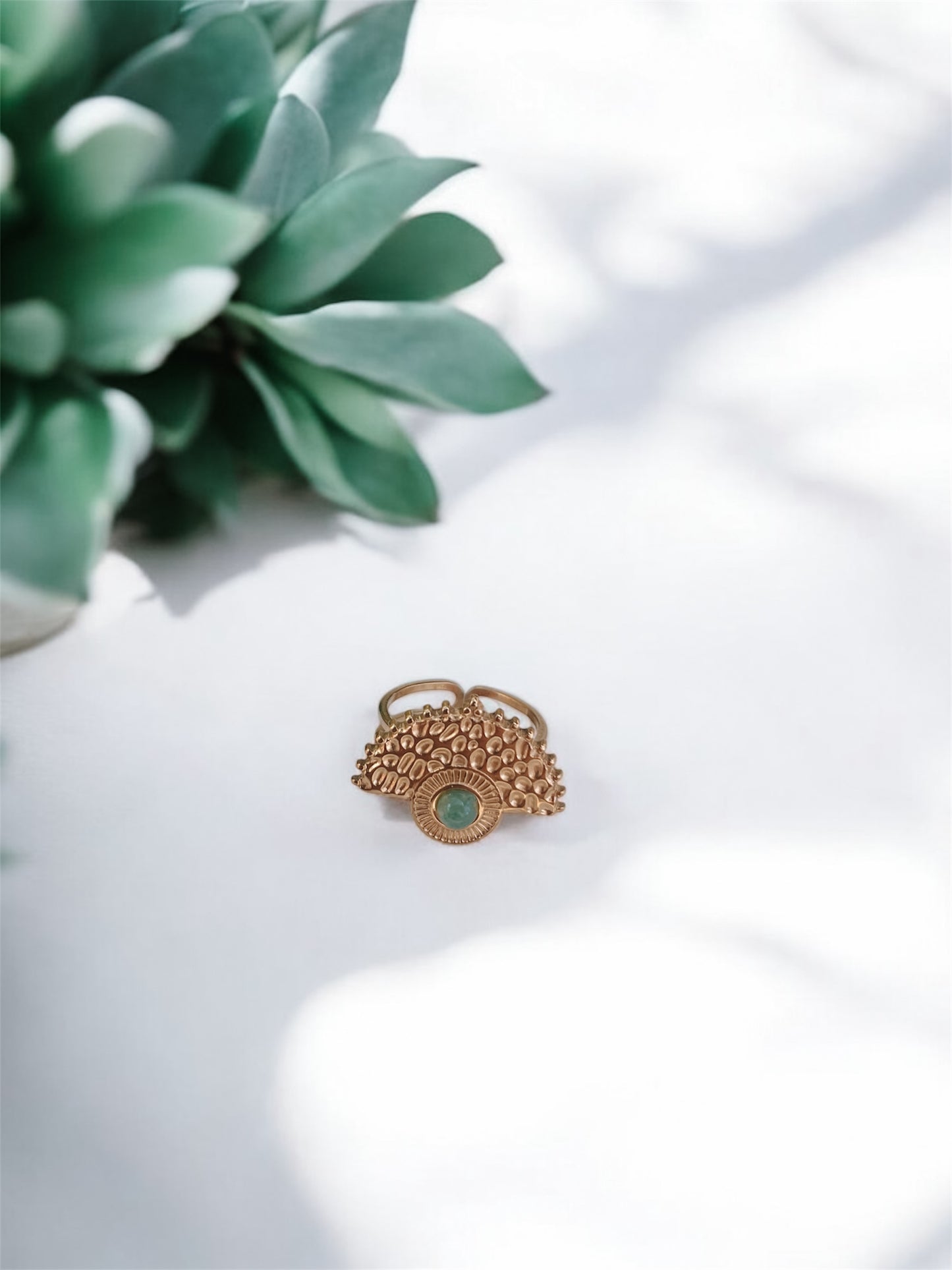 Boho Goldring mit rundem grünen Aventurin-Stein auf weißem Tisch mit Pflanze
