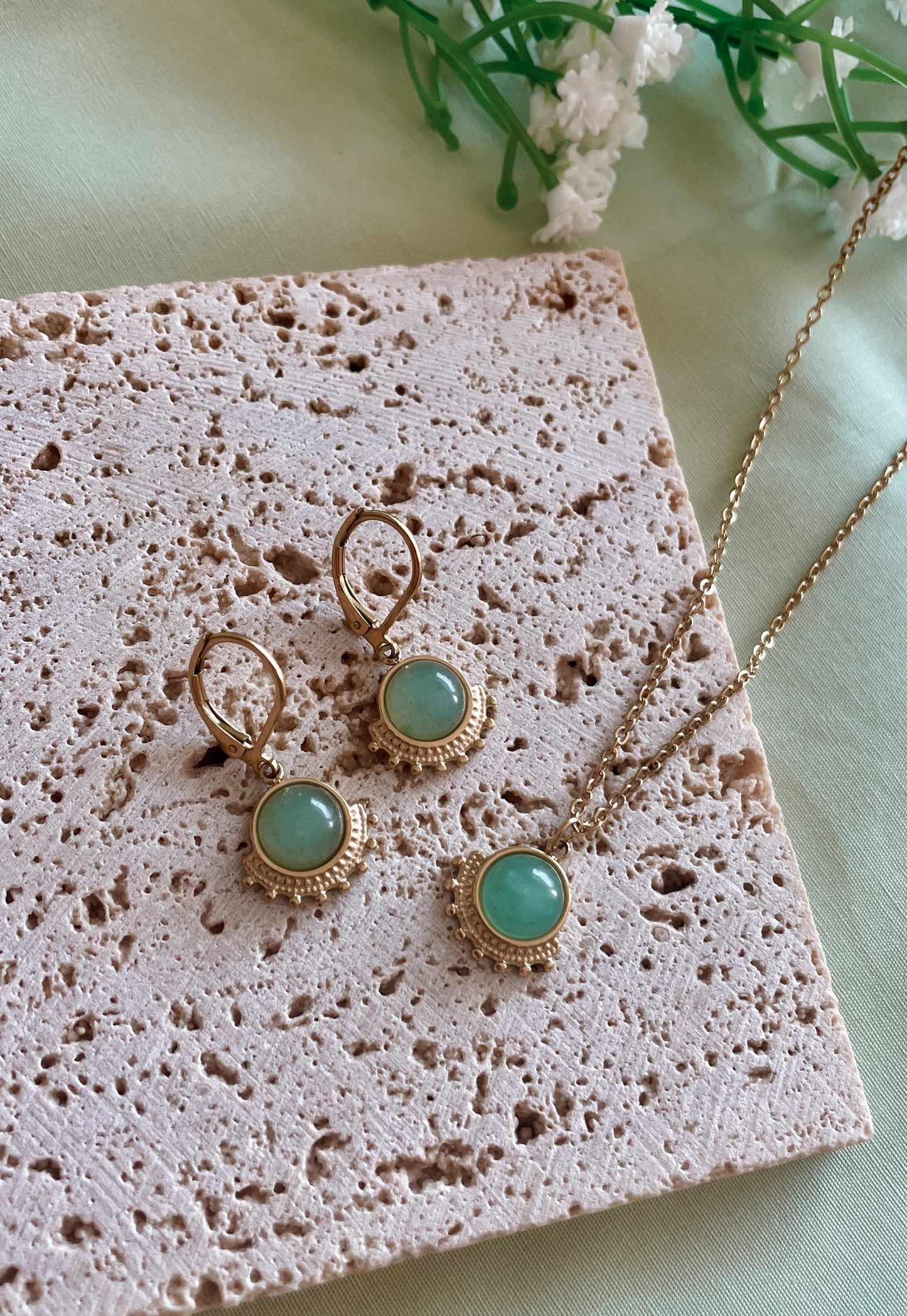Goldenes Schmuckset mit Ohrring und Halskette mit grünen Aventurin Anhängern liegend auf Stein