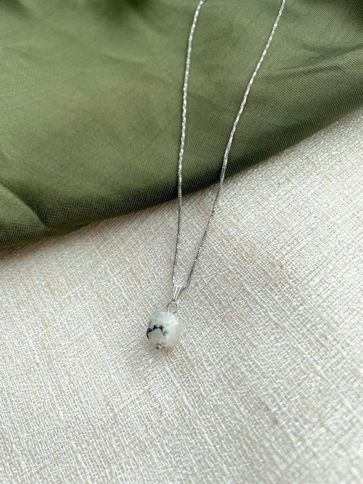 Handgemachte weiße Mondstein-Kette mit würfelförmigen Anhänger in Silber, liegend auf Tuch