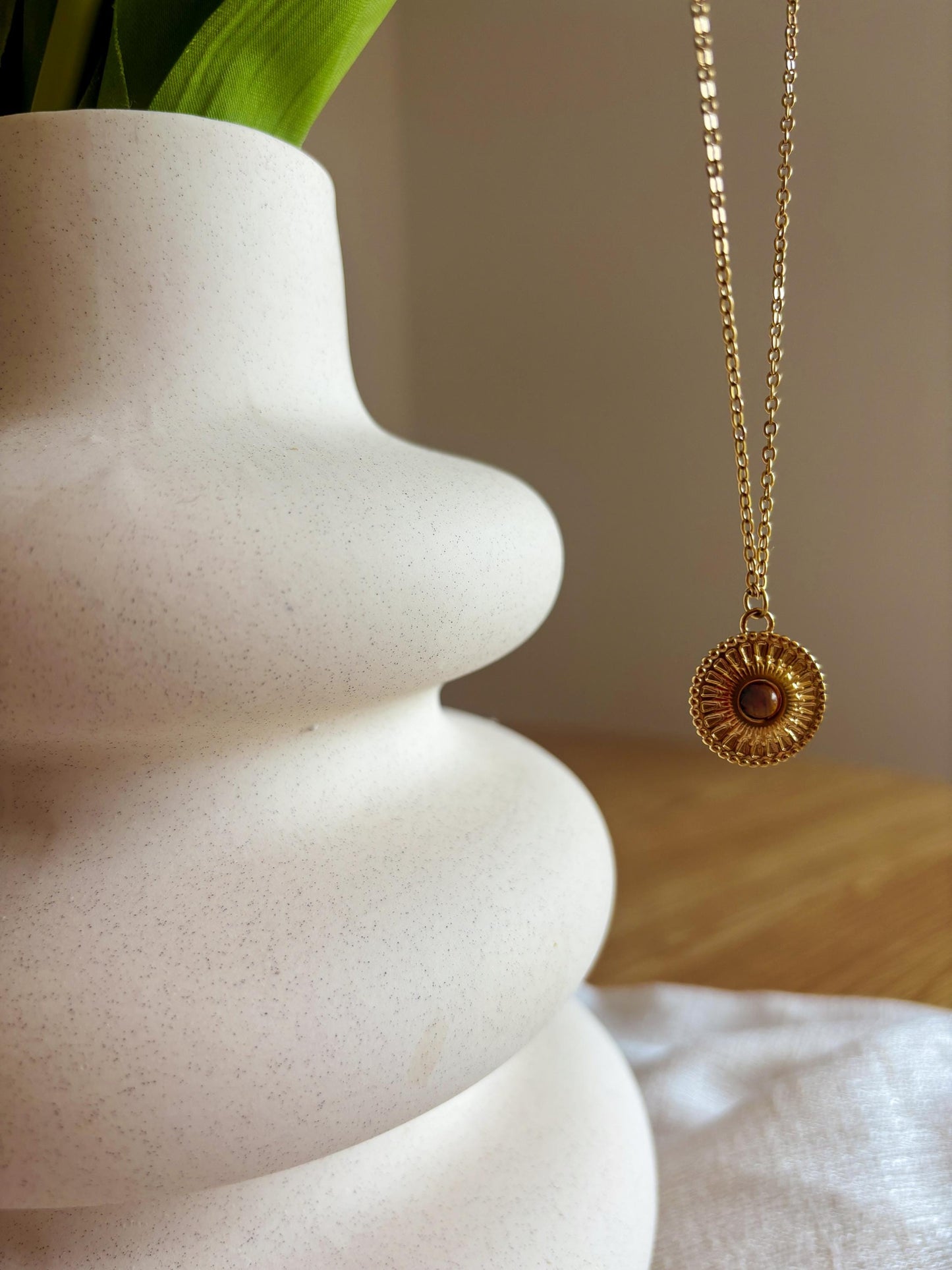 Handgemachte braune Tigerauge-Kette mit ovalem Medaillon Anhänger in Gold, hängend an einer Vase