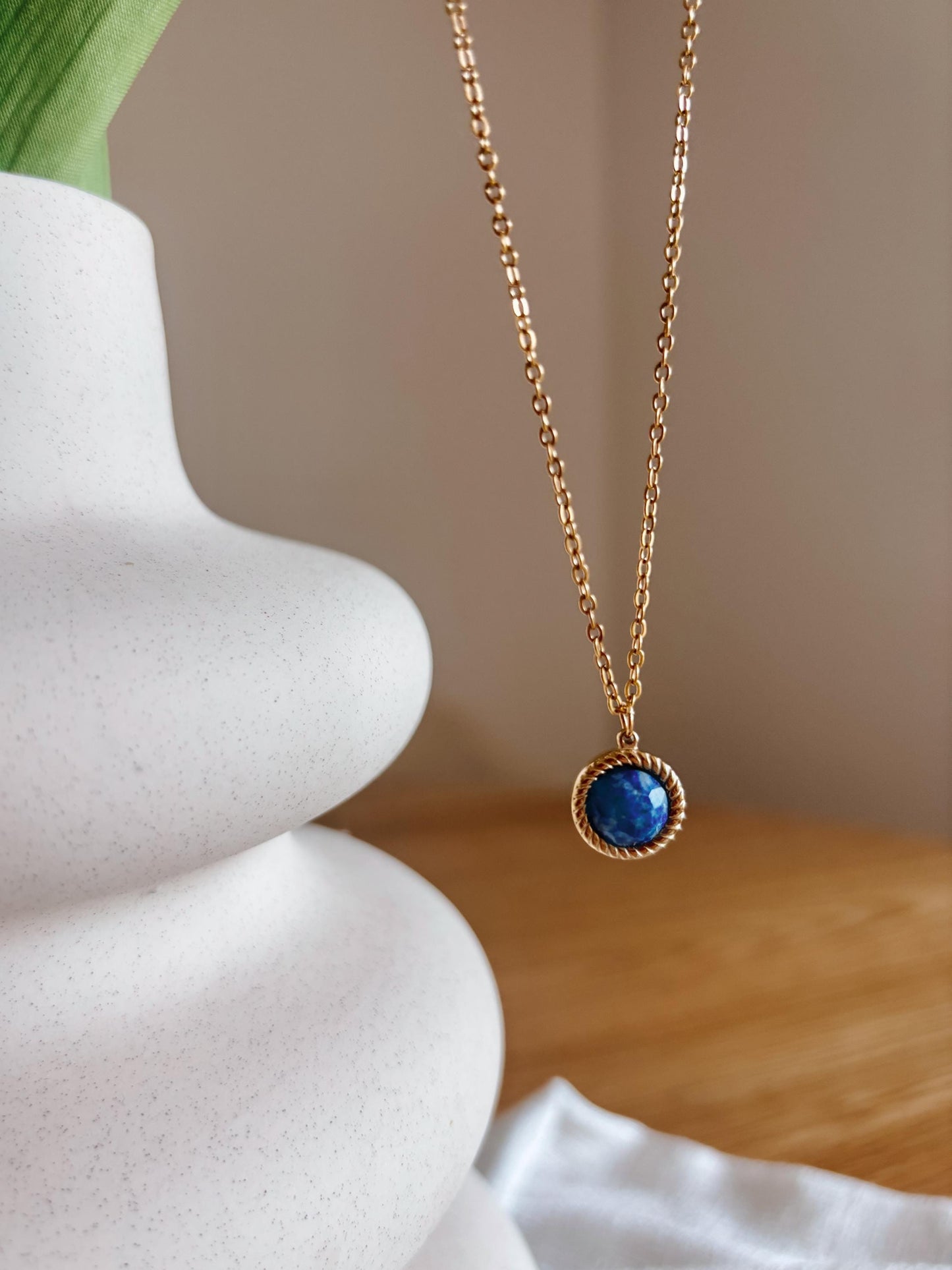 Handgemachte blaue Lapislazuli-Kette mit rundem Anhänger in Gold, hängend an einer Vase