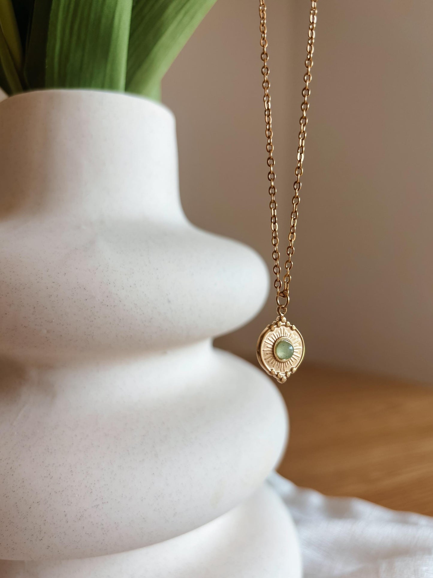 Handgemachte grüne Aventurin-Kette mit rundem Münze Anhänger in Gold, hängend an einer Vase