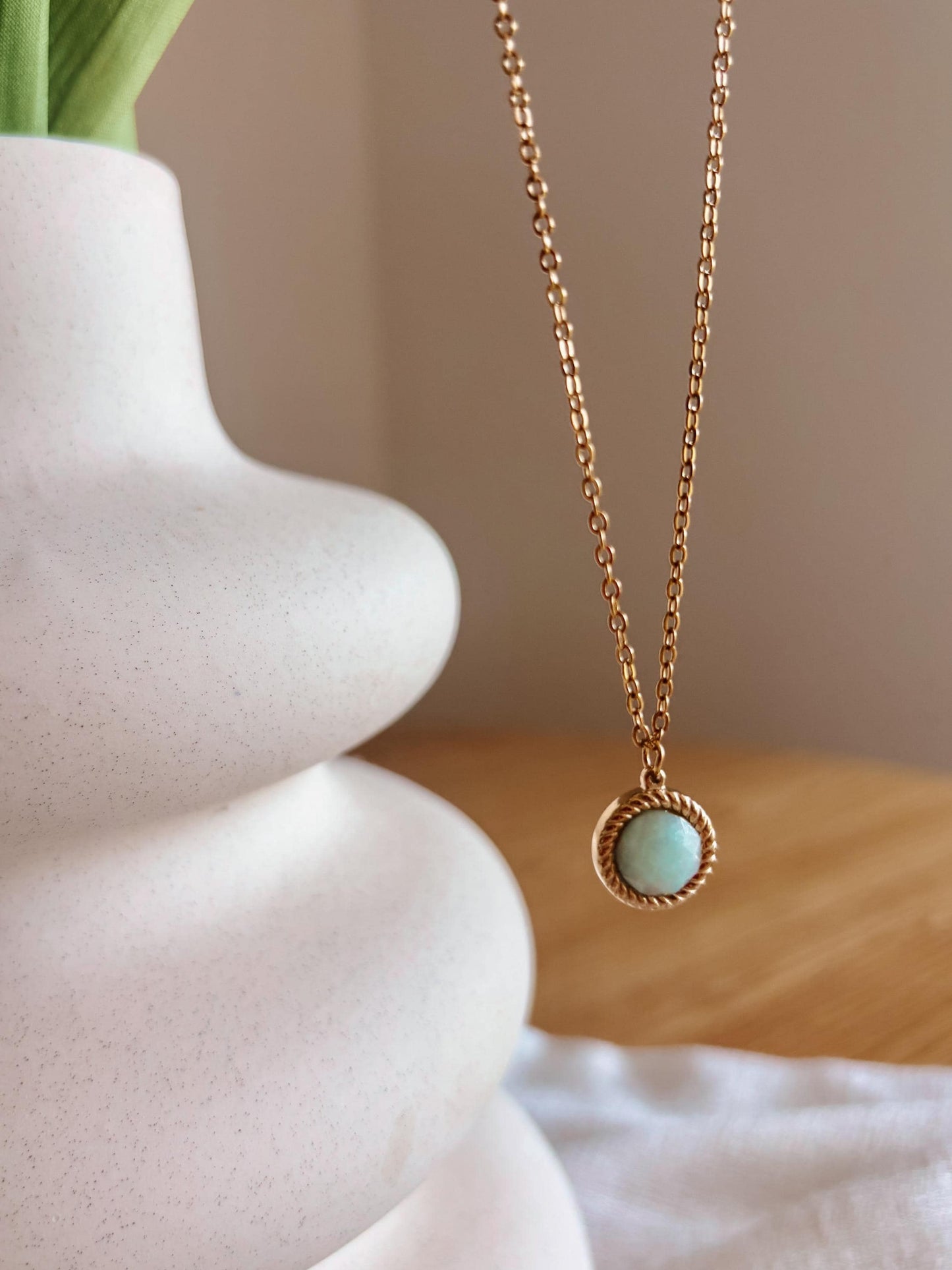 Handgemachte hellblaue Amazonit-Kette mit rundem facettierten Anhänger in Gold, hängend an einer Vase
