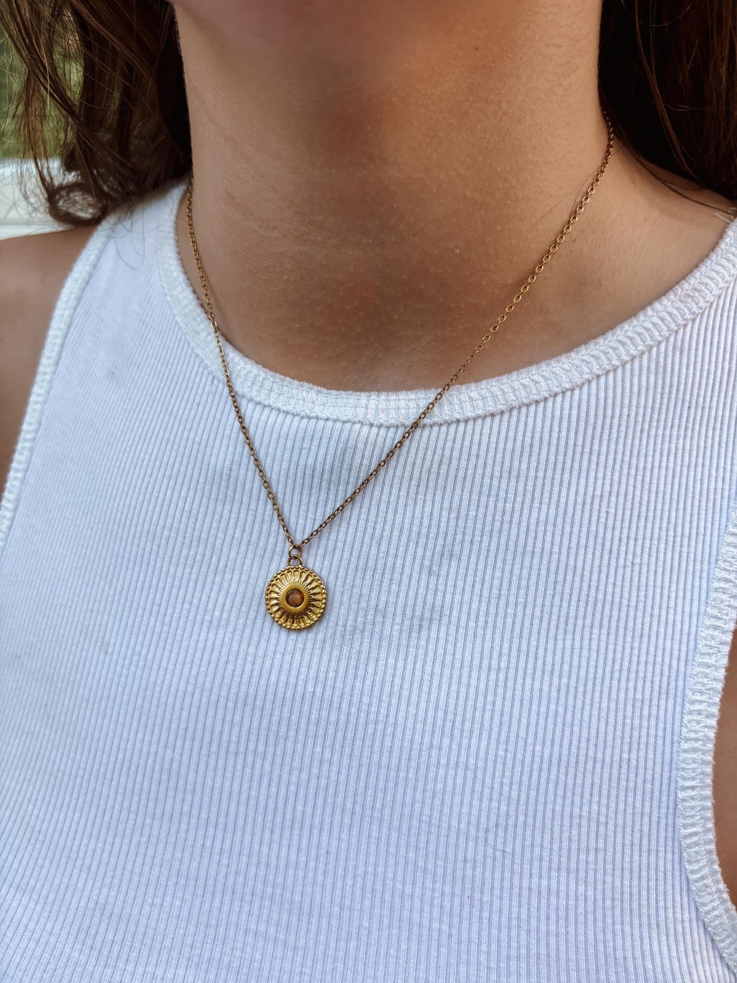 Runder brauner Tigerauge-Anhänger an feiner Medaillon Goldkette, am Dekolleté eines Modells gezeigt.