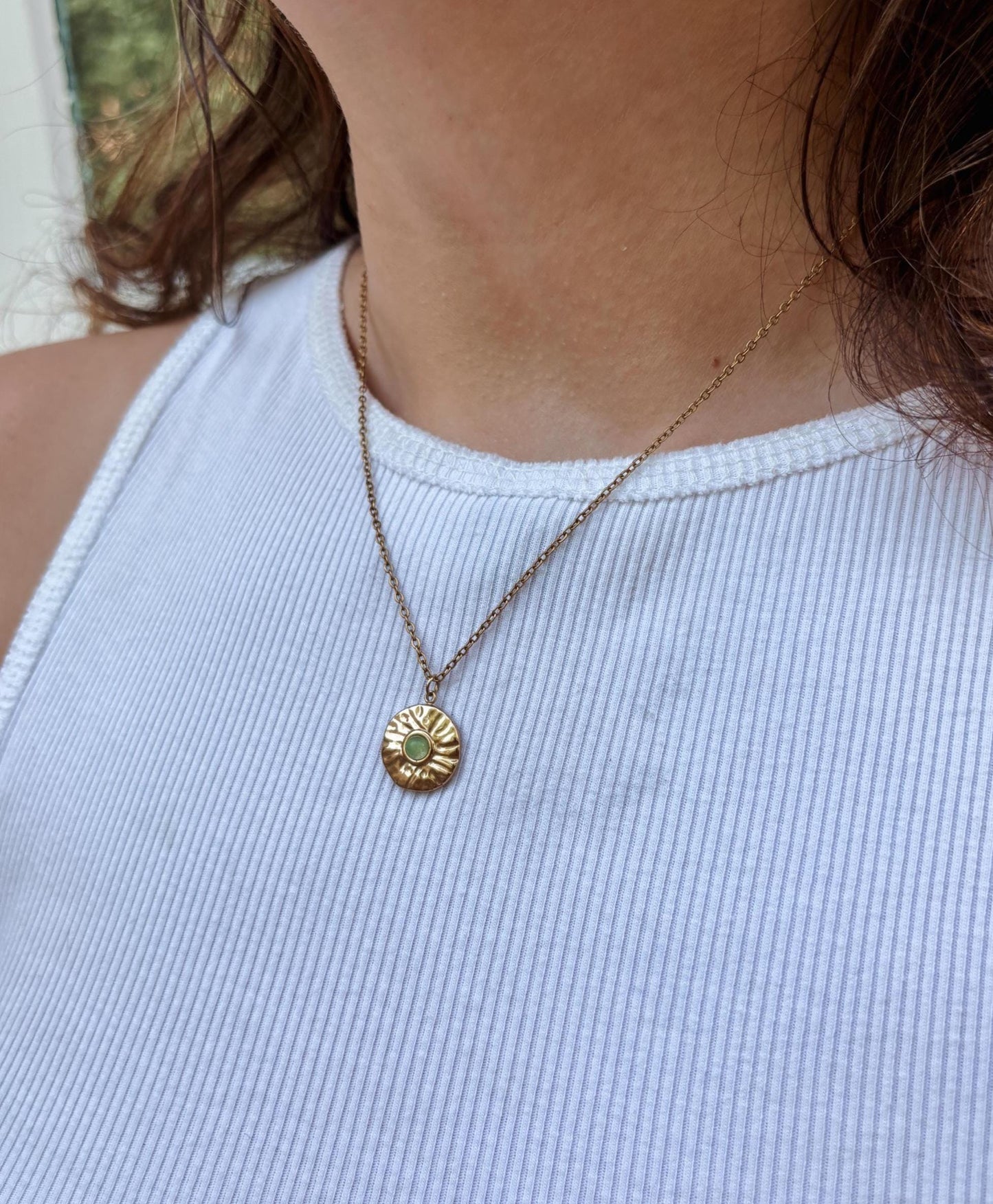 Runder grüner Aventurin Stein an Medaillon Anhänger an feiner Goldkette, am Dekolleté eines Modells gezeigt.
