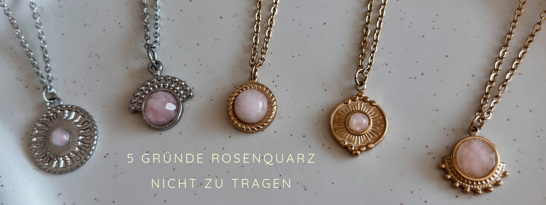Fünf Halsketten mit Rosenquarz-Anhängern in verschiedenen Metallfassungen auf hellem Hintergrund.