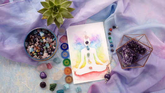 Meditierende Figur mit Chakra-Symbolen, umgeben von Kristallen und Halbedelsteinen auf buntem Tuch.
