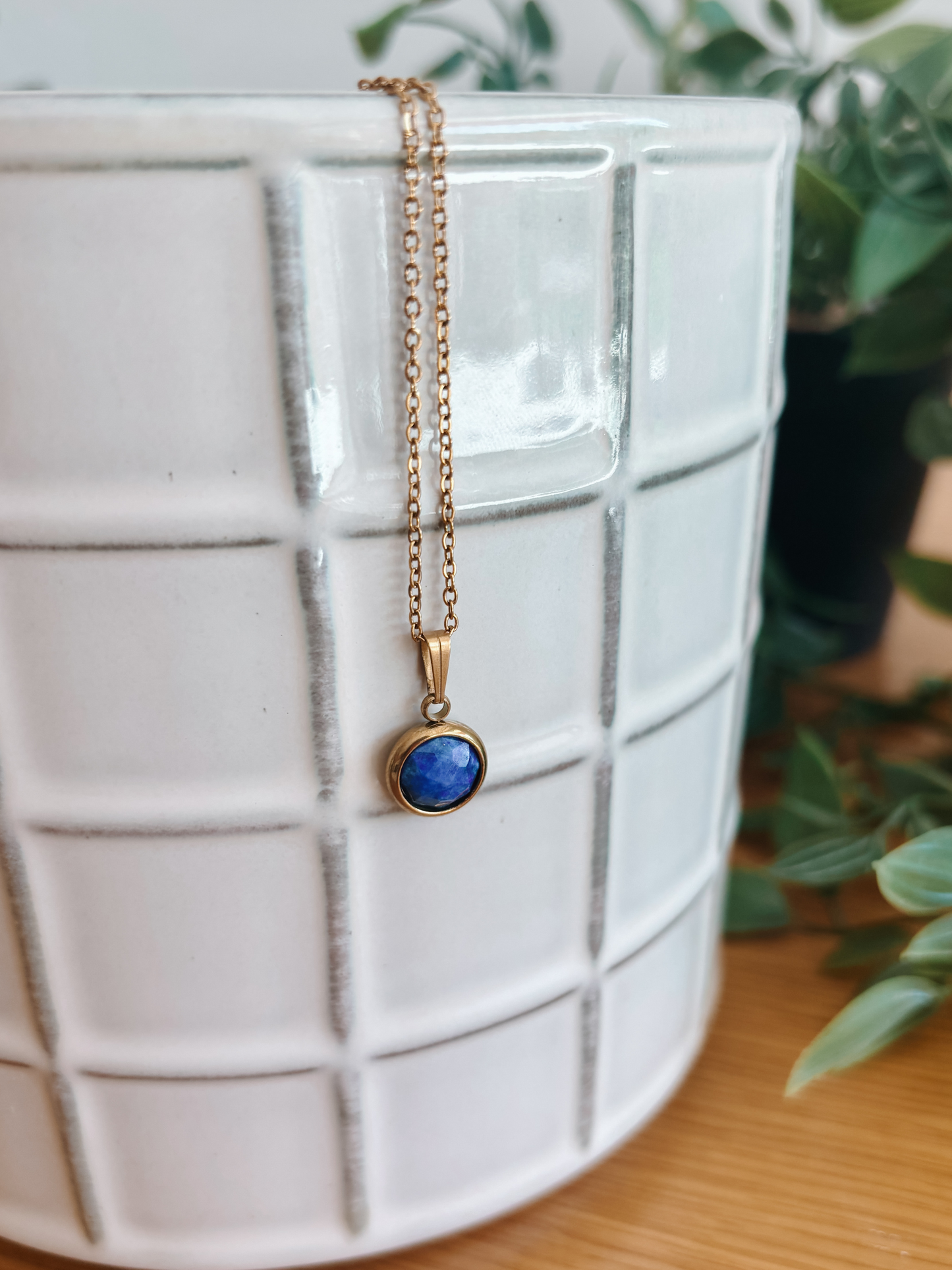 Handgemachte blaue Lapis-Lazuli-Kette mit rundem Anhänger in Gold, hängend an einer Vase