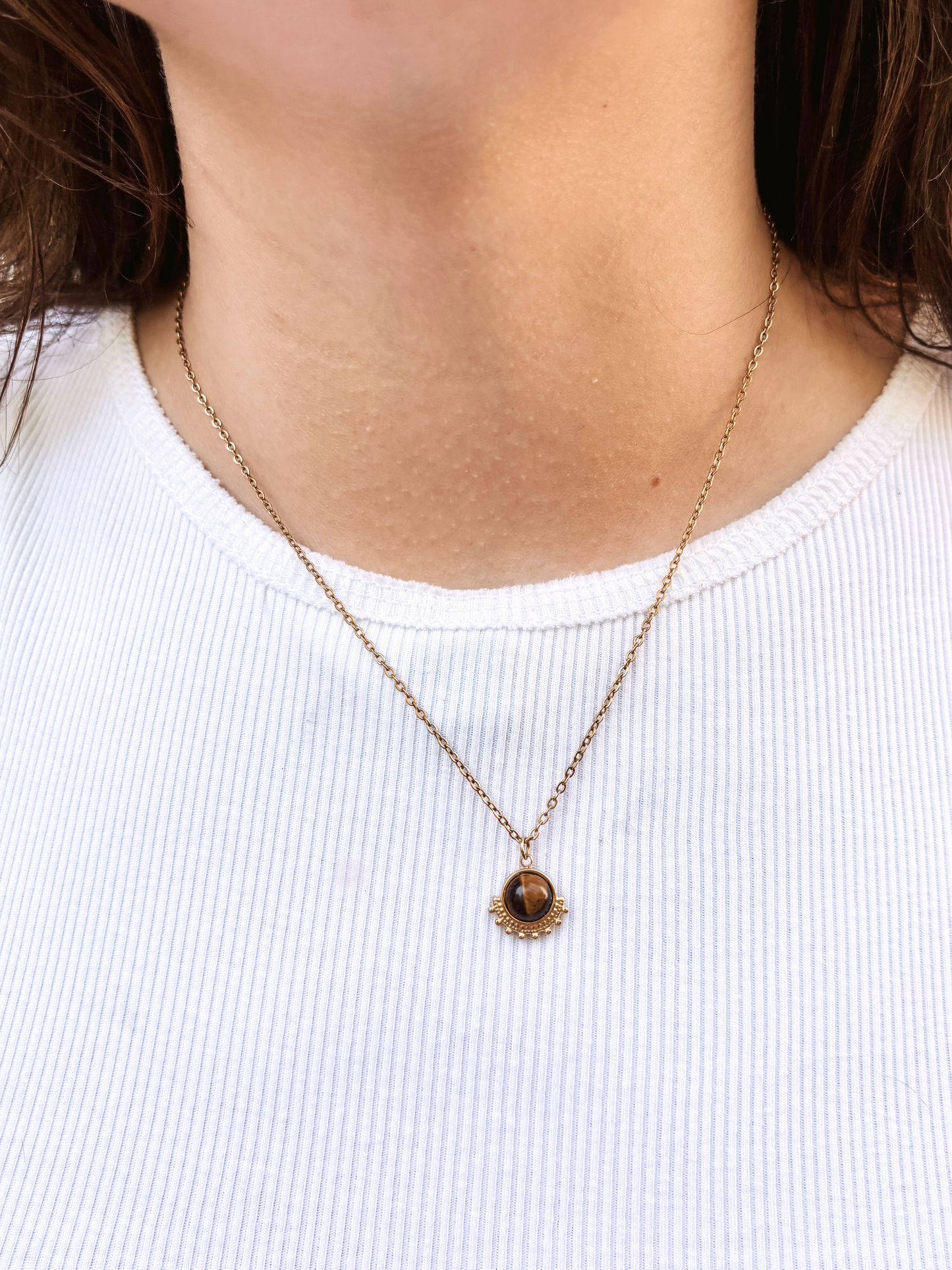 Kette mit goldenem verziertem Anhänger mit braunem Tigerauge Stein am Hals eines Models