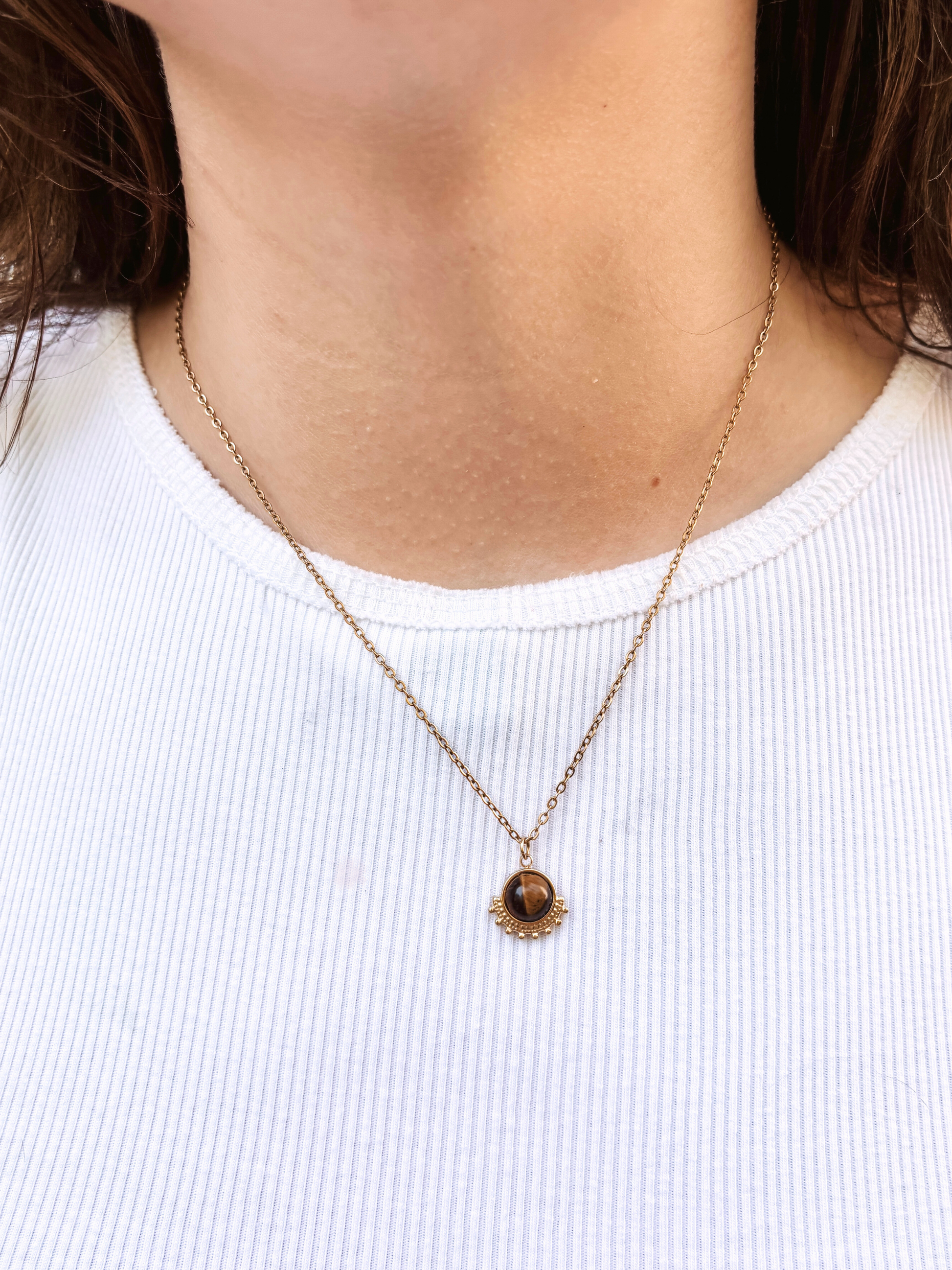 Kette mit goldenem verziertem Anhänger mit braunem Tigerauge Stein am Hals eines Models