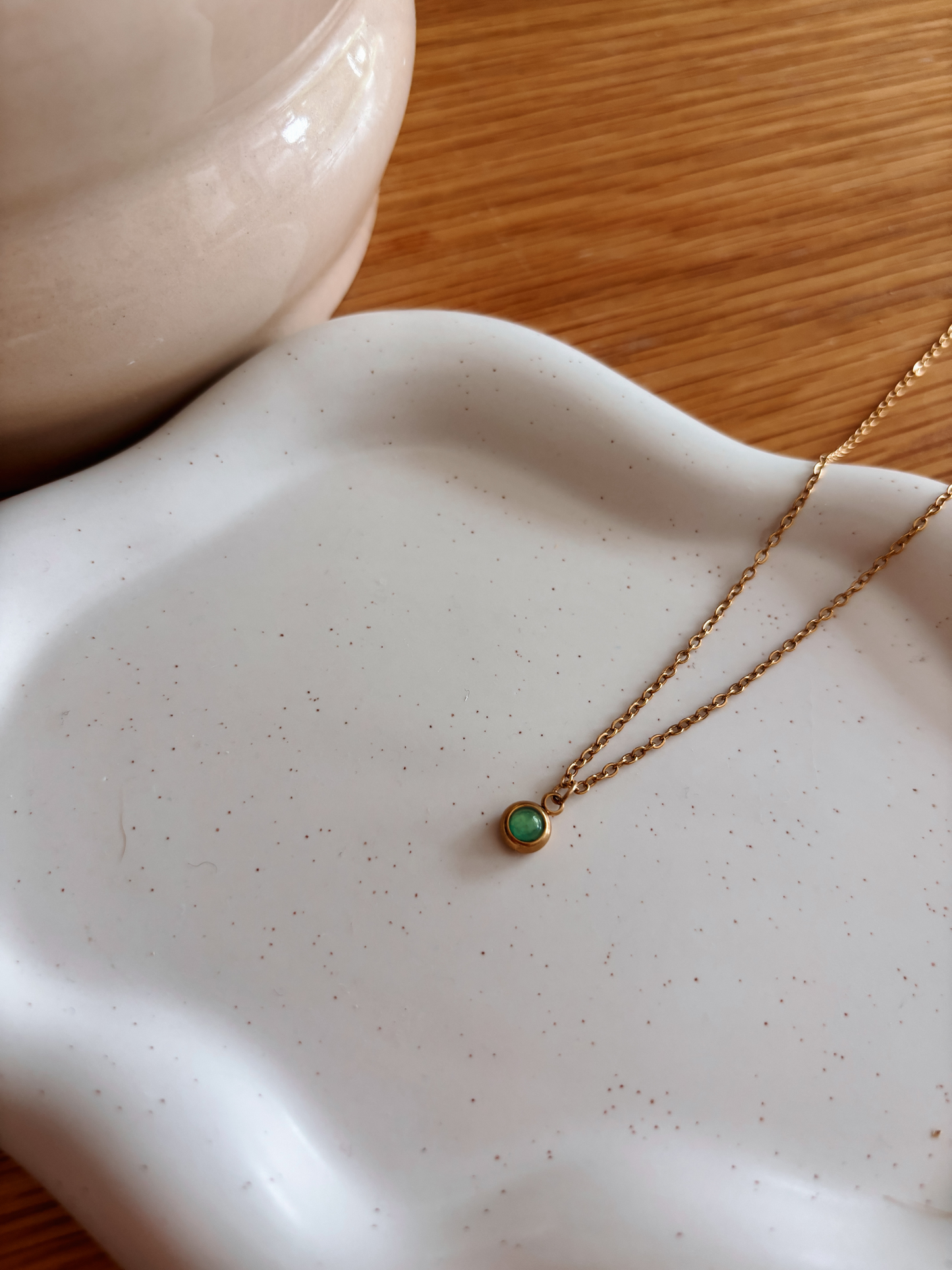 Handgemachte grüne Aventurin-Kette mit winzigem runden Anhänger in Gold, liegend auf weißem Tablett