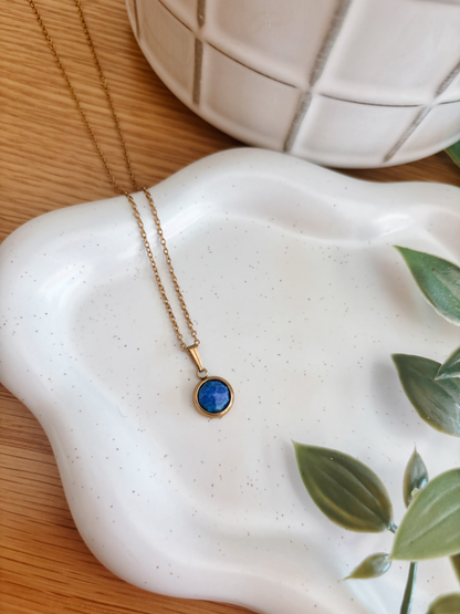 Handgemachte blaue Lapis-Lazuli-Kette mit rundem Anhänger in Gold, liegend auf Tablett