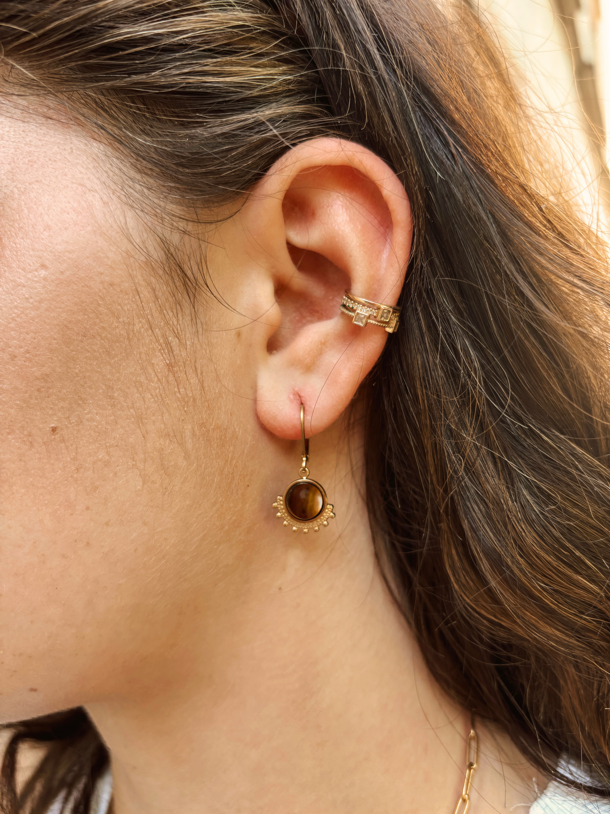 Ohrring mit goldenem verziertem Anhänger mit braunem Tigerauge Stein am Ohr eines Models, Detailaufnahme