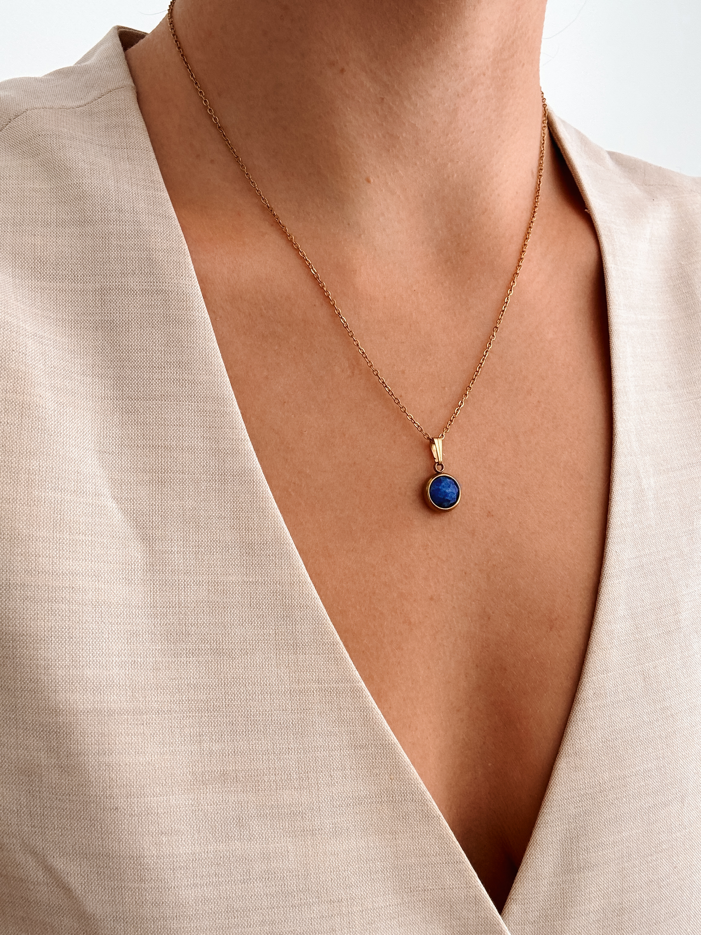 Runder blauer Lapis-Lazuli-Anhänger an feiner Goldkette, am Dekolleté eines Modells gezeigt.