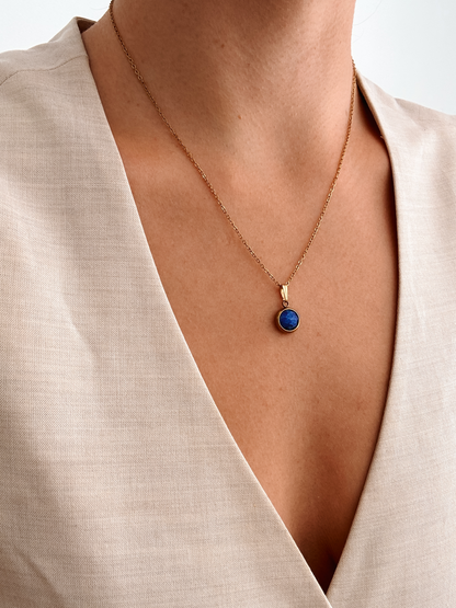 Runder blauer Lapis-Lazuli-Anhänger an feiner Goldkette, am Dekolleté eines Modells gezeigt.