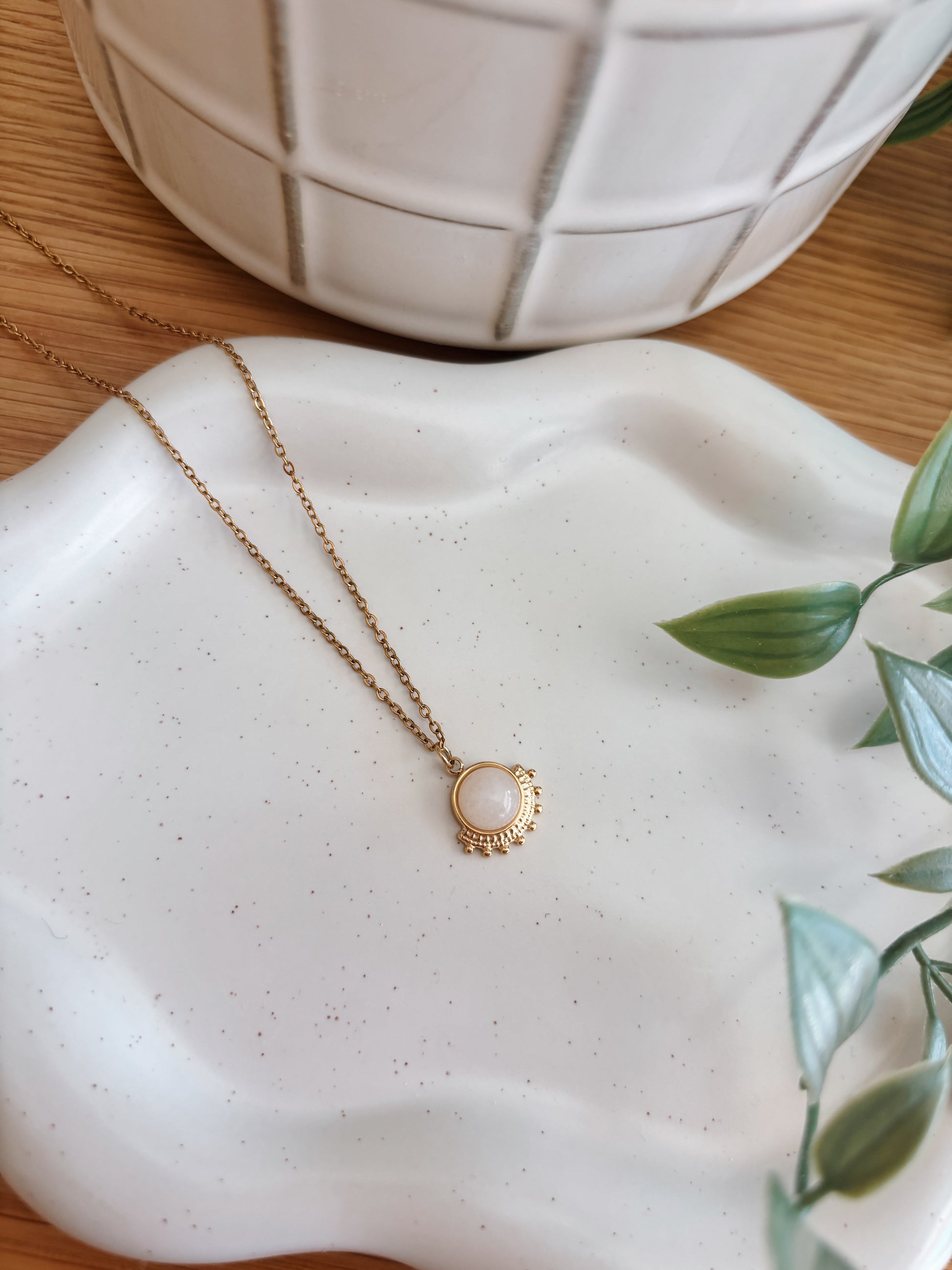 Handgemachte weiße Jade-Kette mit rundem Anhänger in Gold mit Zacken,  liegend auf Tablett