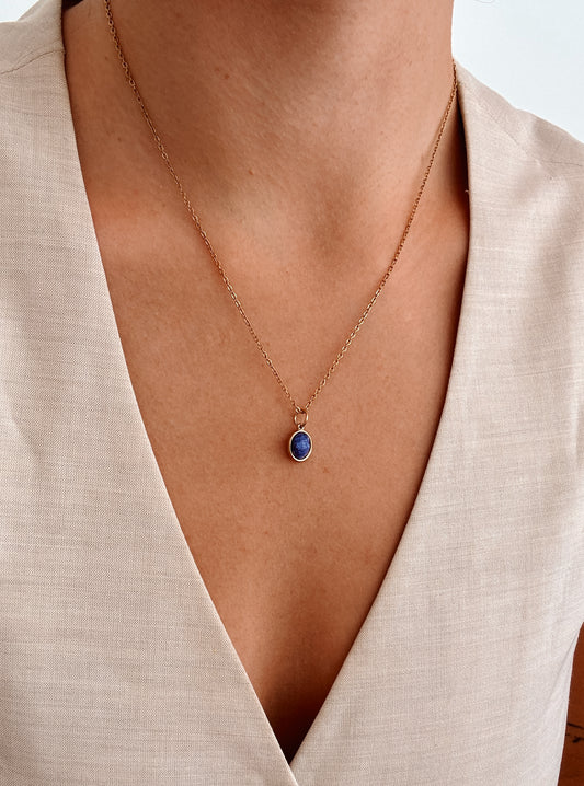 Ovaler blauer Lapis-Lazuli-Anhänger an feiner Goldkette, am Dekolleté eines Modells gezeigt.