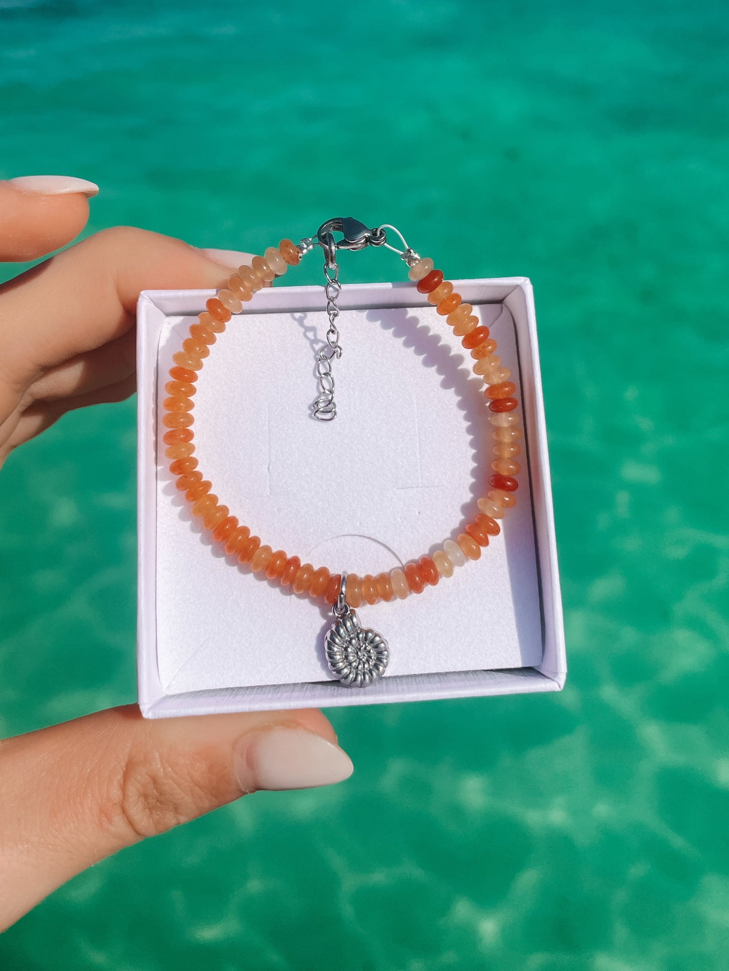 oranges Karneol-Perlenarmband in Silber mit Muschel-Schnecke Anhänger liegend in weißer Schmuckbox