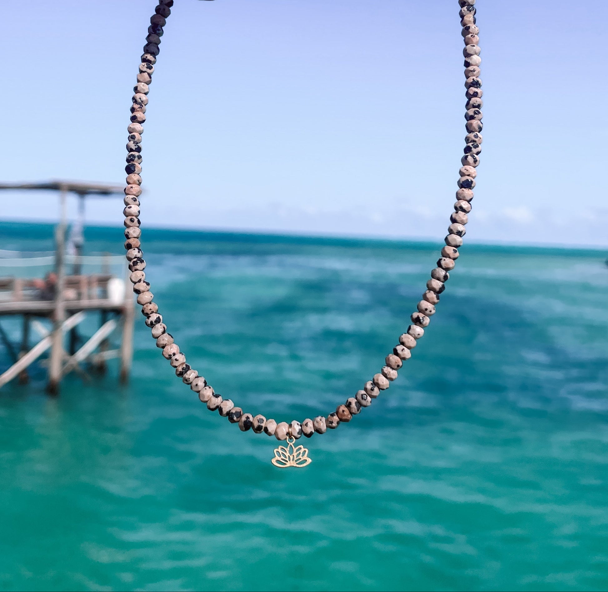 gepunktete Dalmatiner Jaspis-Perlenkette mit goldenem Lotusblume Anhänger hängend vor Meer