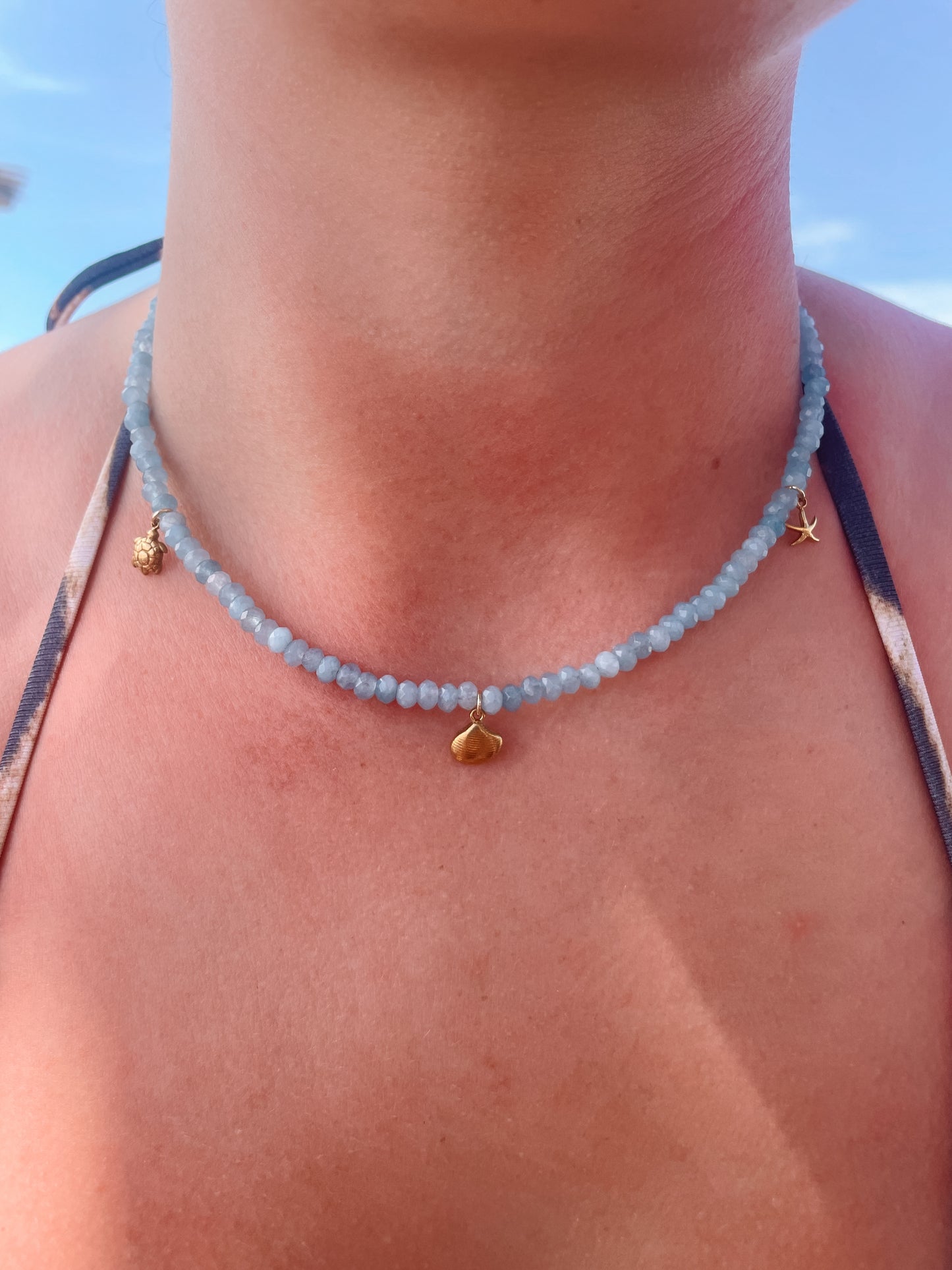 Blaue Jade-Perlenkette mit maritimen Gold Anhängern am Dekollete eines Modells