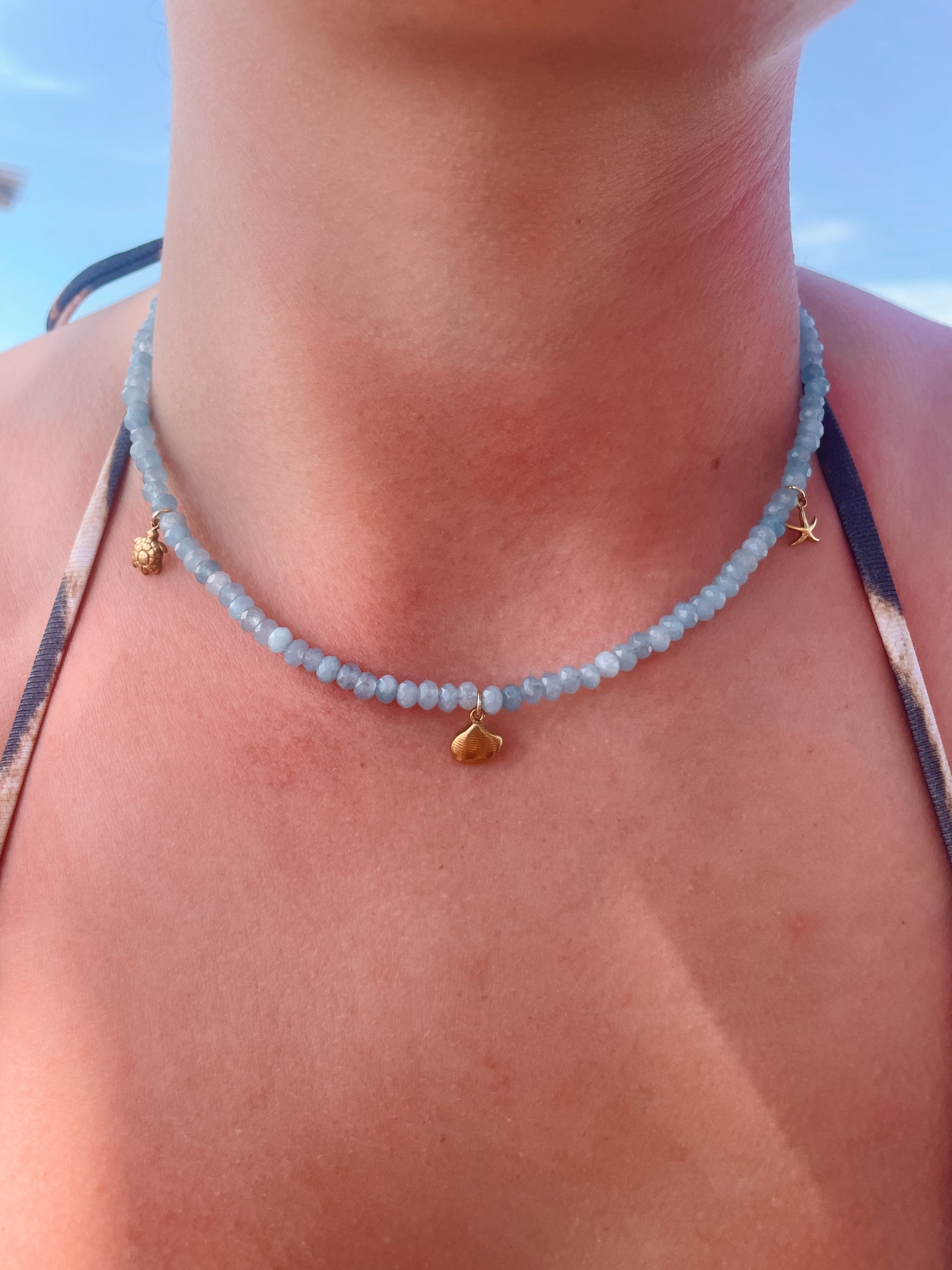 Blaue Jade-Perlenkette mit maritimen Gold Anhängern am Dekollete eines Modells