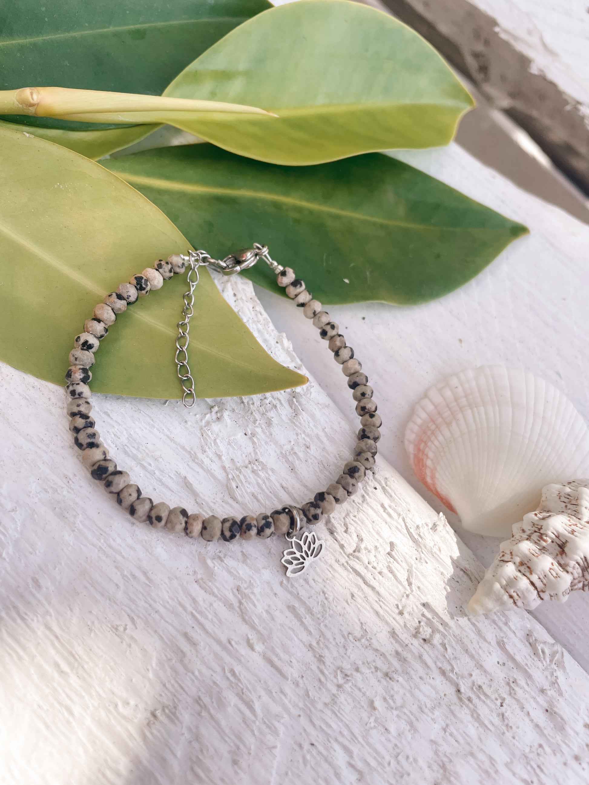gepunktetes Dalmatiner Jaspis-Perlenarmband in Silber mit Lotusblume Anhänger liegend auf weißem Holz