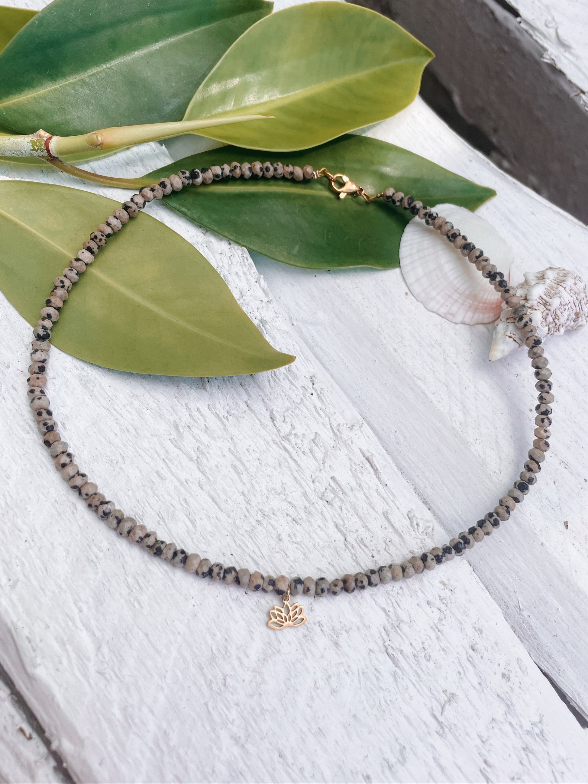 gepunktete Dalmatiner Jaspis-Perlenarmkette in Gold mit Lotusblume Anhänger liegend auf weißem Holz