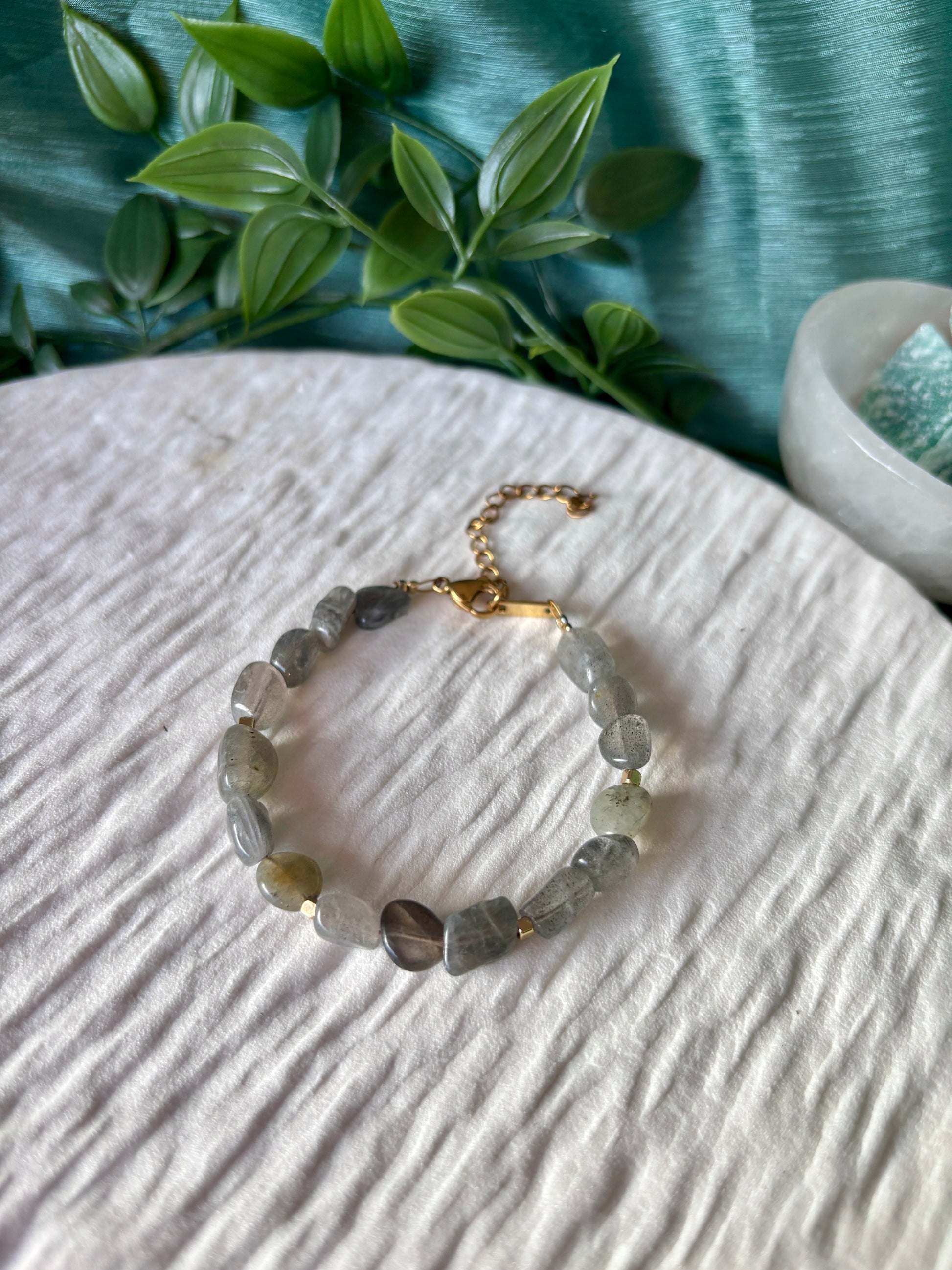 Goldenes Labradorit Perlenarmband mit grauen Natursteinen liegend auf weißem Tablett, Ansicht von oben