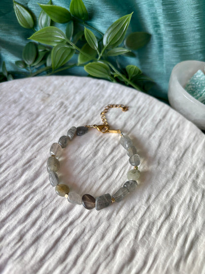 Goldenes Labradorit Perlenarmband mit grauen Natursteinen liegend auf weißem Tablett, Ansicht von oben