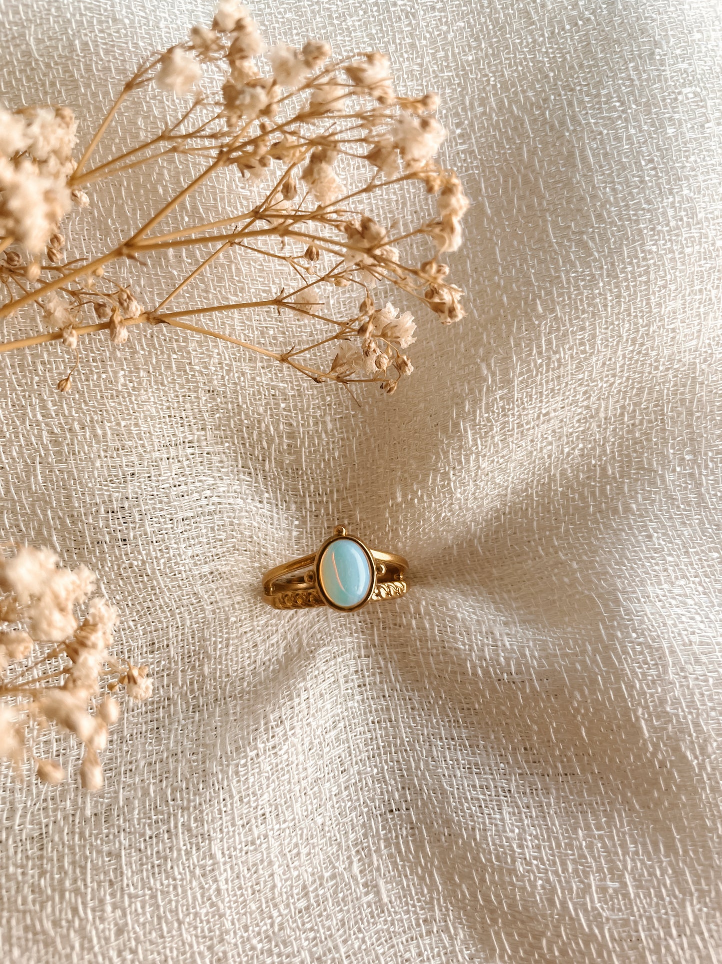 Boho Goldring mit ovalem weiß-blauen Opalith-Stein auf weißem Tuch mit Blumen