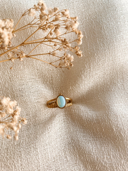 Boho Goldring mit ovalem weiß-blauen Opalith-Stein auf weißem Tuch mit Blumen