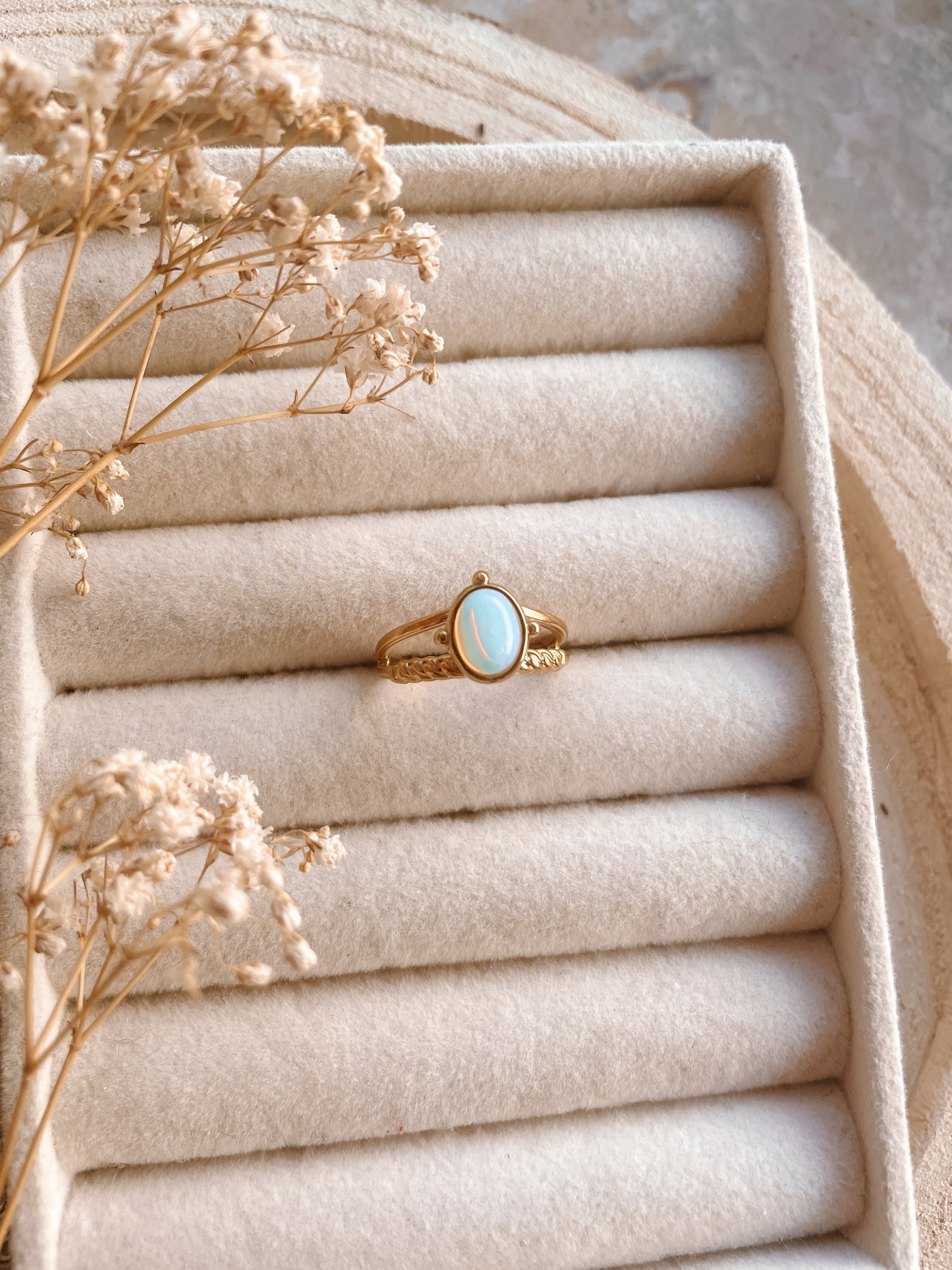 Goldring mit ovalem blauen Opalith-Stein auf Schmucktablett mit Blumen