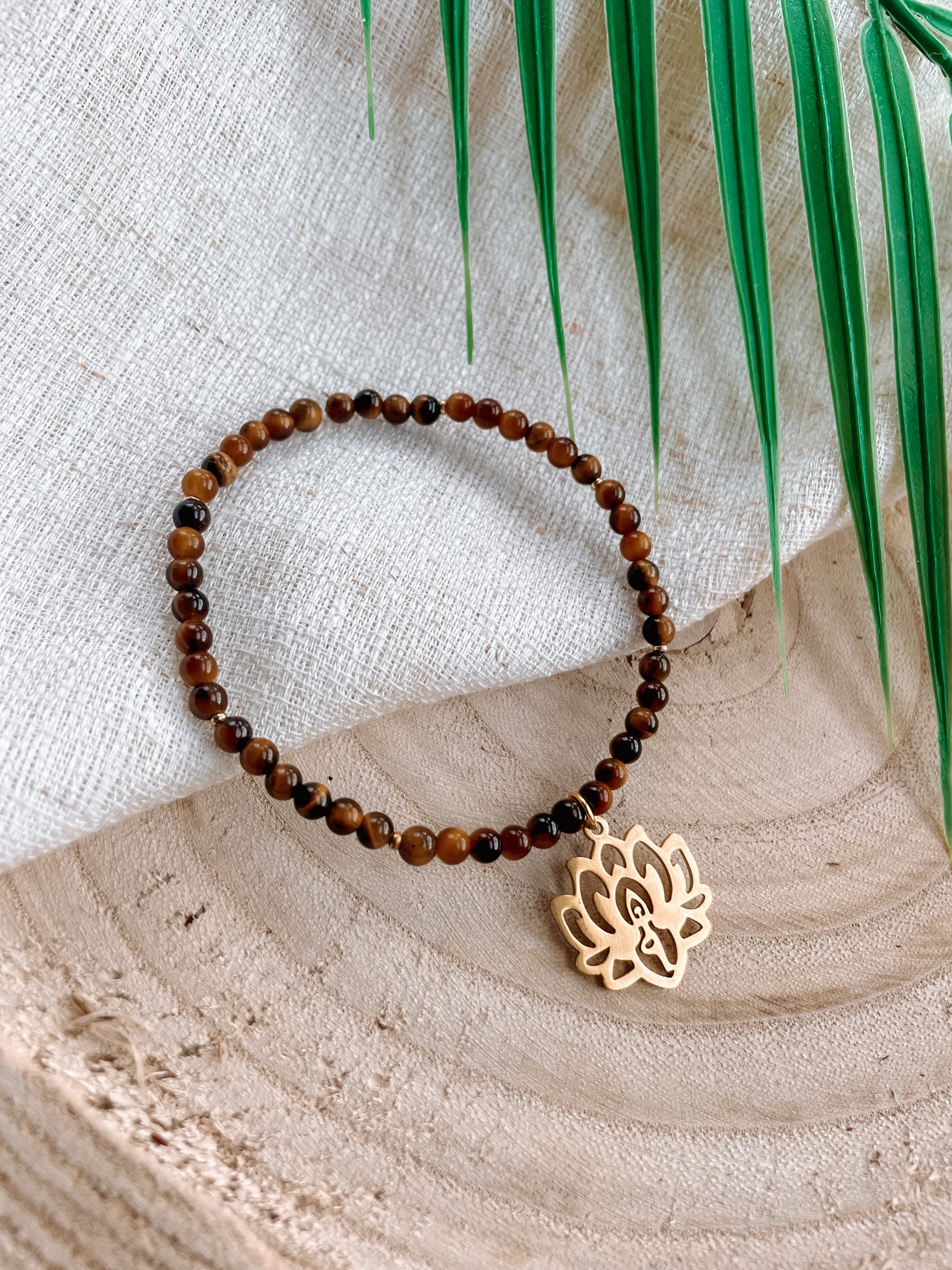 braunes Tigerauge-Perlenarmband in Gold mit Yoga Lotusblume Anhänger liegend auf weißem Tuch