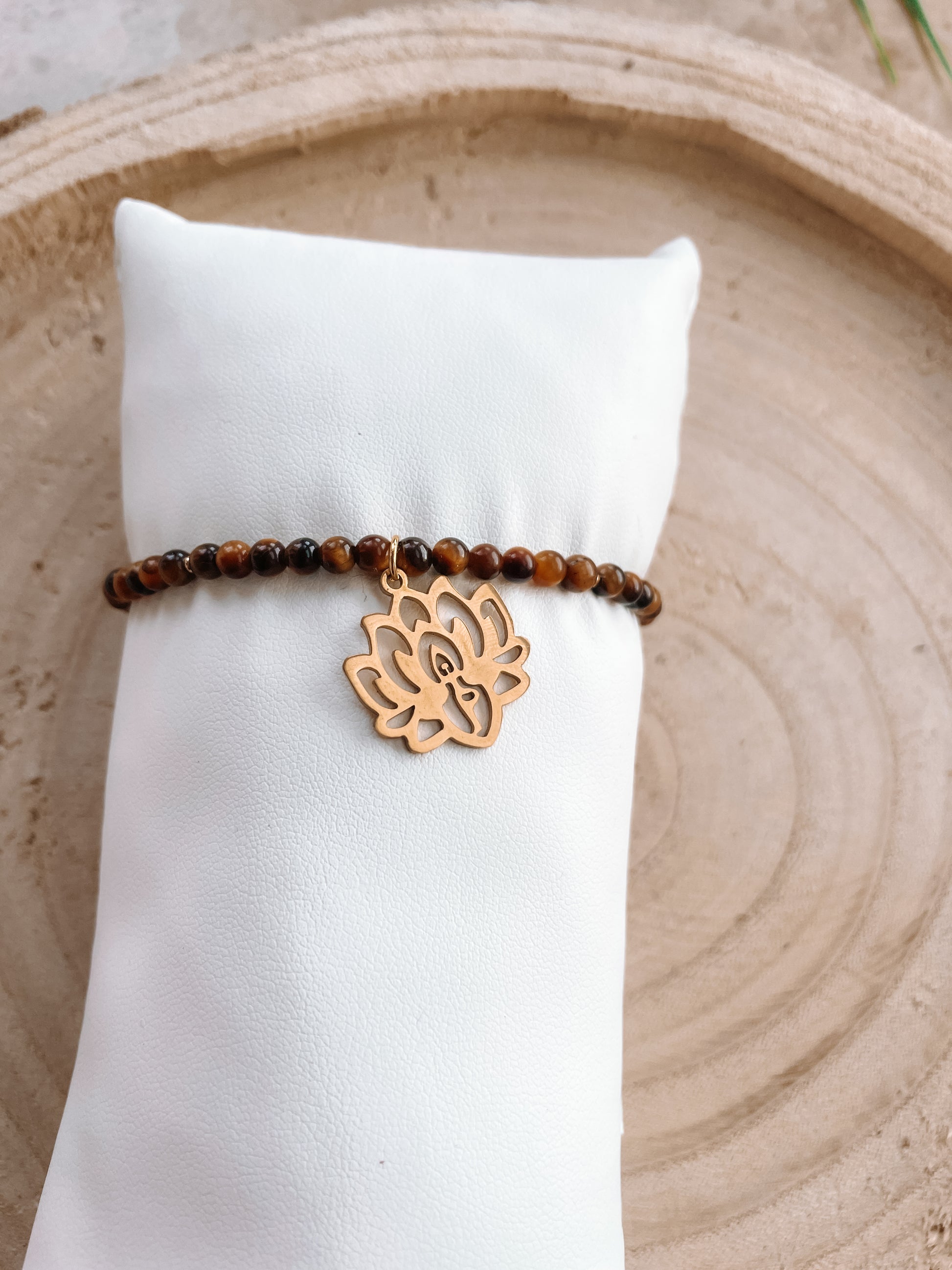 braunes Tigerauge-Perlenarmband in Gold mit Yoga Lotusblüte Anhänger an weißem Schmuckkissen