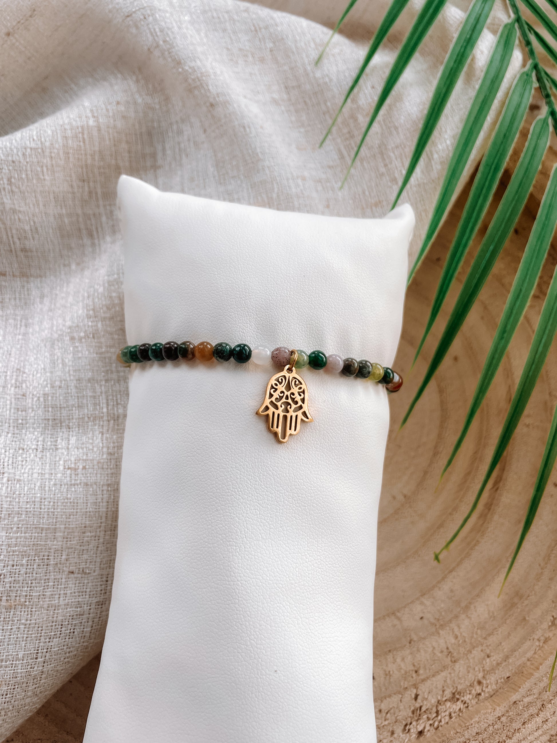 Buntes Turmalin-Perlenarmband mit goldenem Hand von Fatima Anhänger auf weißem Kissen
