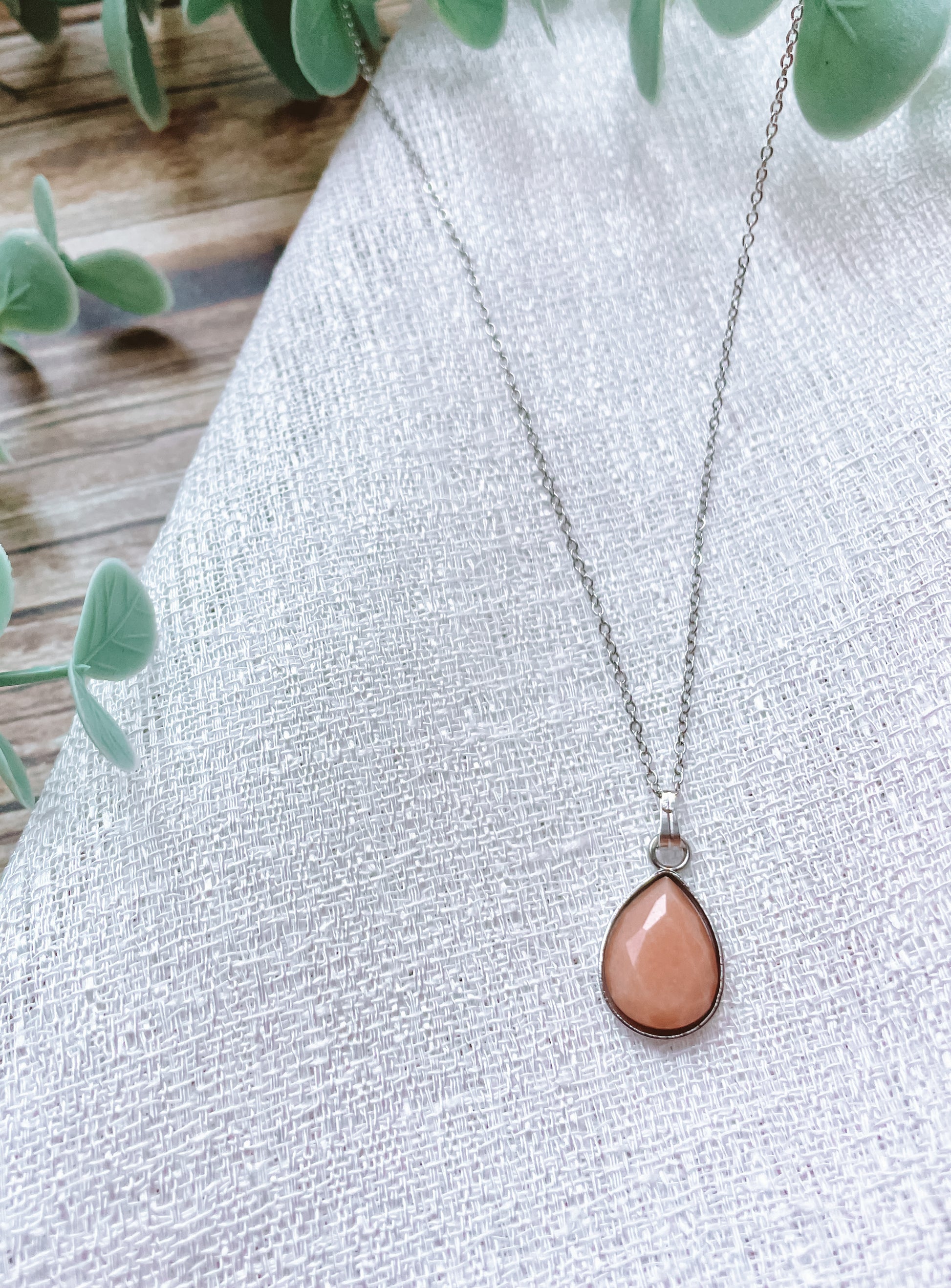 Handgemachte rosa Sonnenstein-Kette mit Tropfen Anhänger in Silber,  liegend auf weißem Tuch