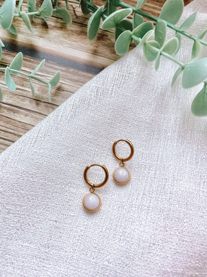 Goldene Creolen-Ohrringe mit runden, weißen Jade-Steinen auf weißem Tuch