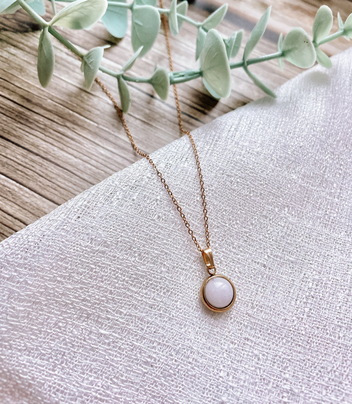 Handgemachte weiße Jade-Kette mit rundem Anhänger in Gold,  liegend auf weißem Tuch