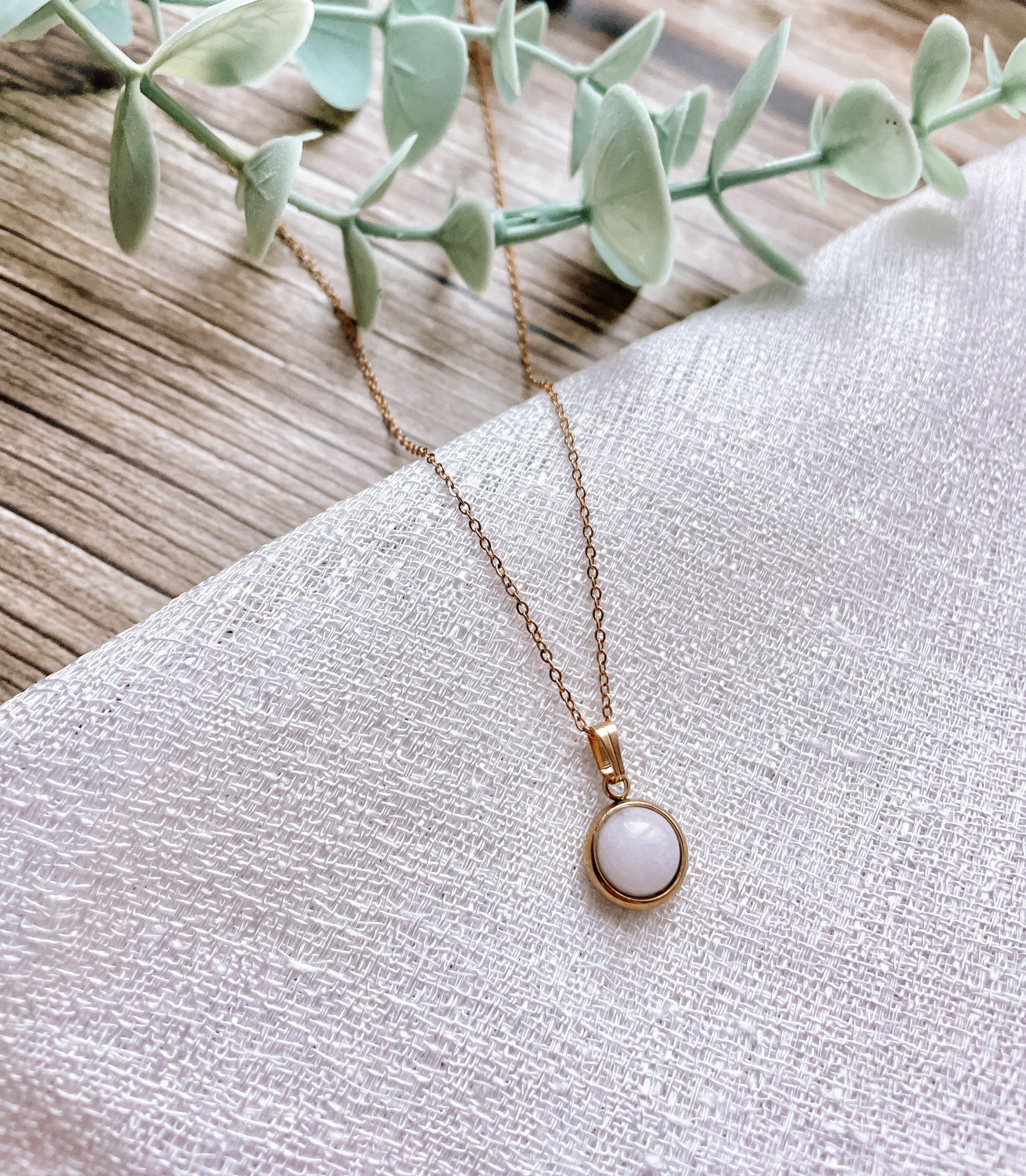 Handgemachte weiße Jade-Kette mit rundem Anhänger in Gold,  liegend auf weißem Tuch