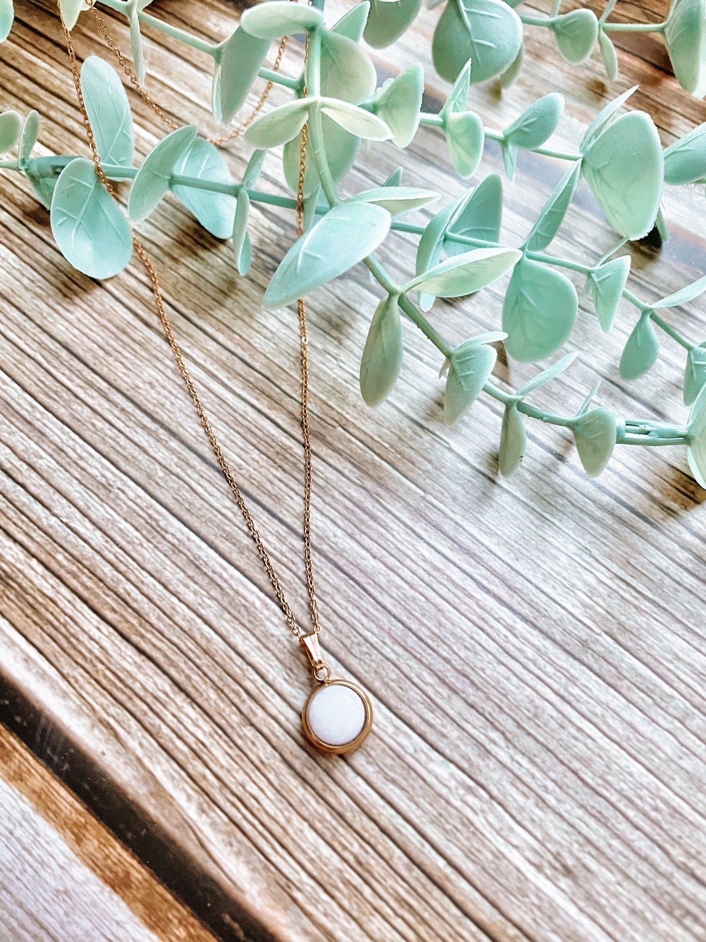 Handgemachte weiße Jade-Kette mit rundem Anhänger in Gold,  liegend auf Holz